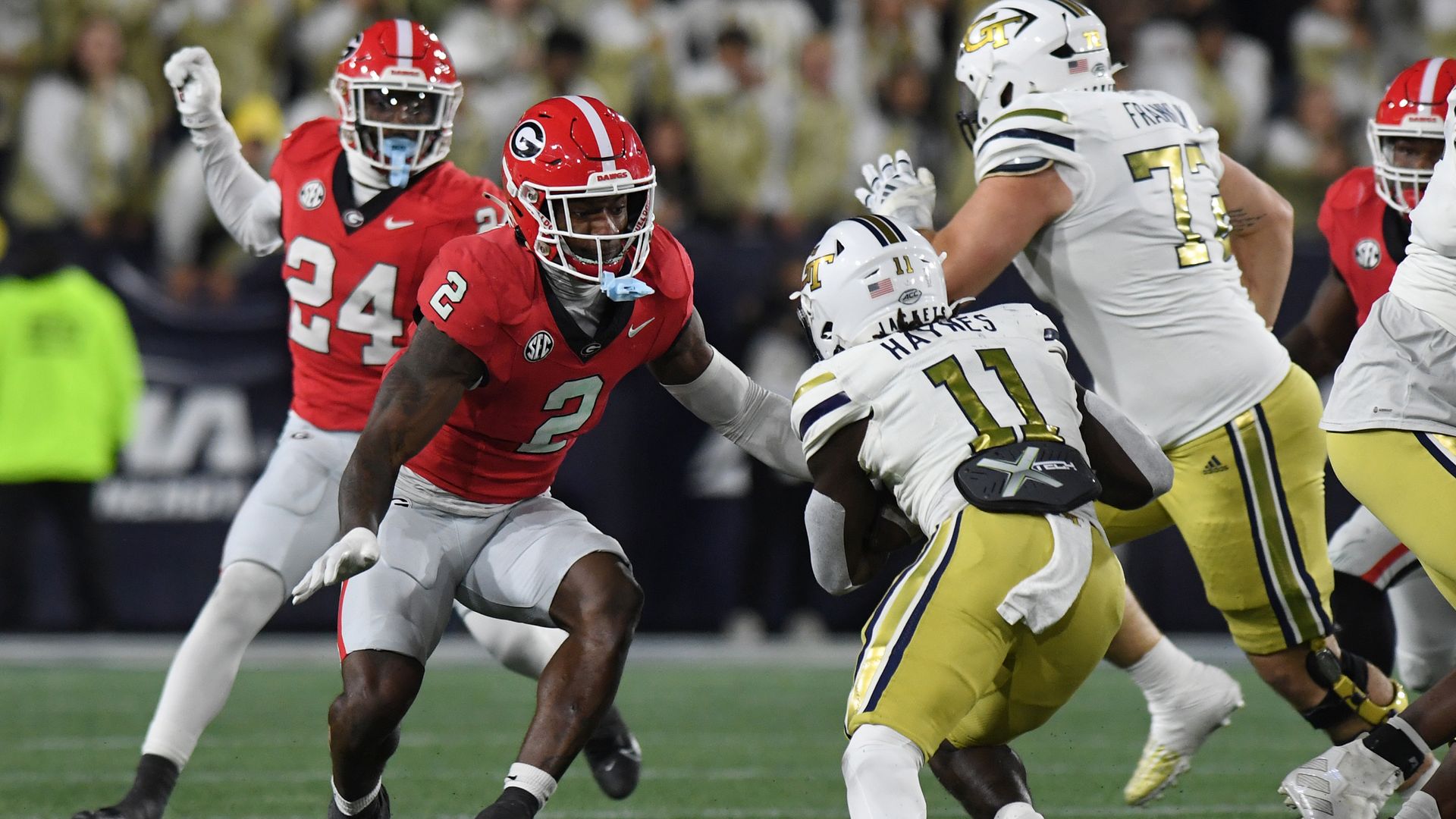 A man in a red football uniform prepares to tackle a man in a white and gold uniform