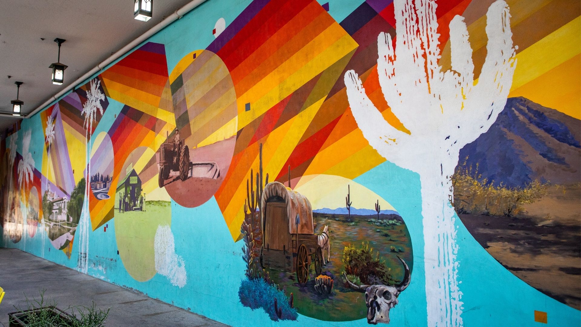 A vibrant mural featuring scenes of desert landscapes, cacti and historic imagery in bold colors.