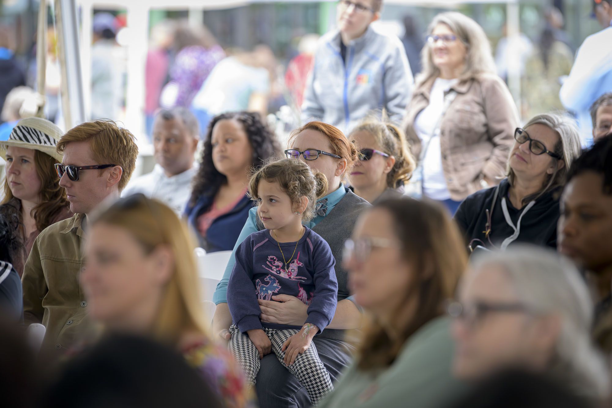 A crowd of people at the Books in Bloom festival centers around a woman holding a child 