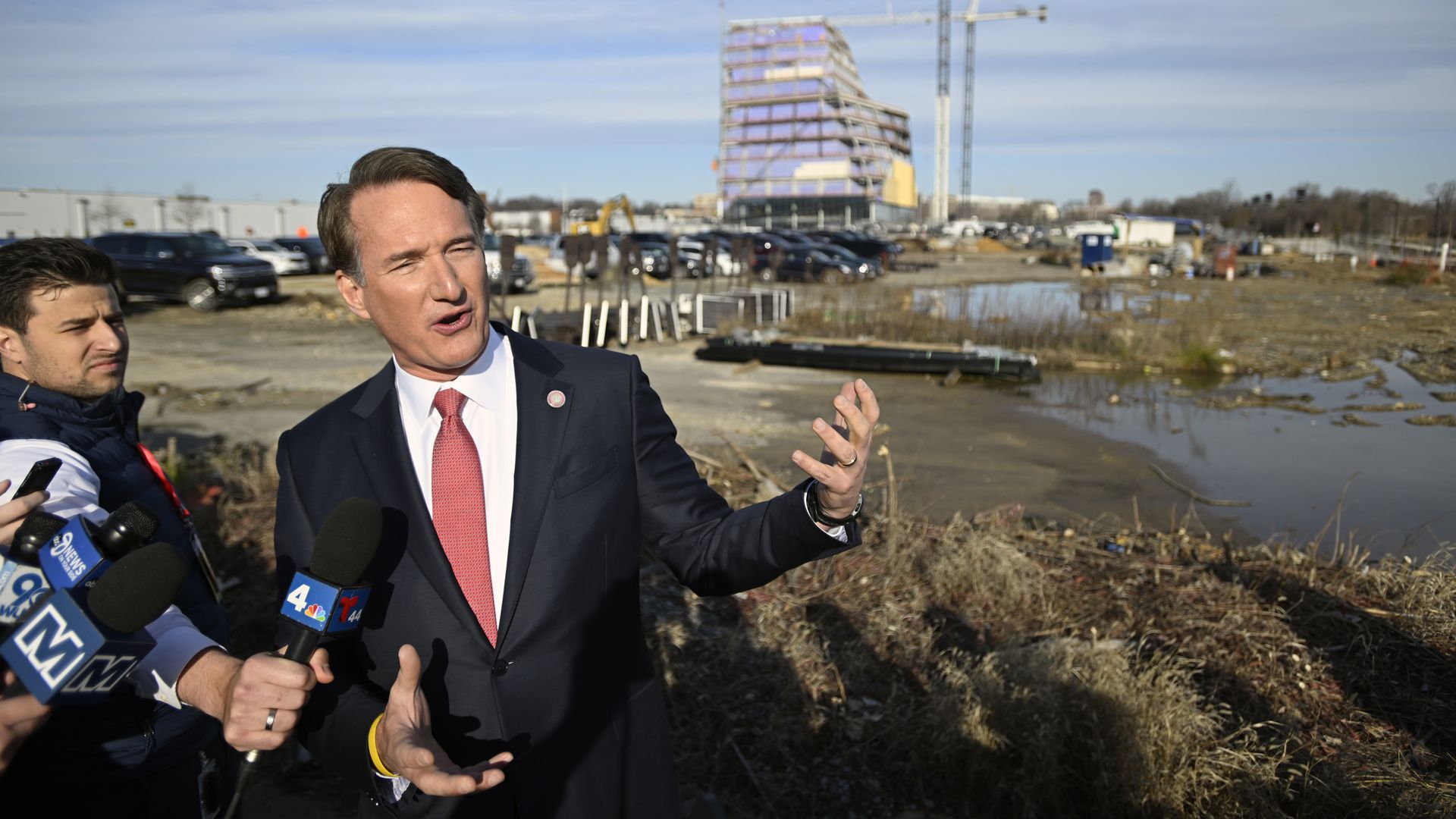 The Virginia governor stands in a suit and a tie in front of a construction site.