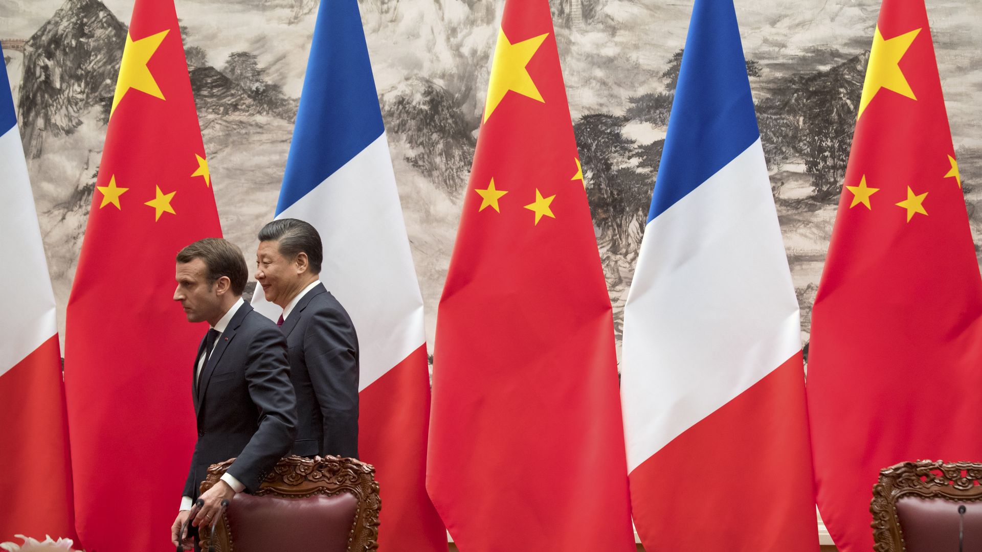 Macron and Xi walk out of a room decorated with French and Chinese flags