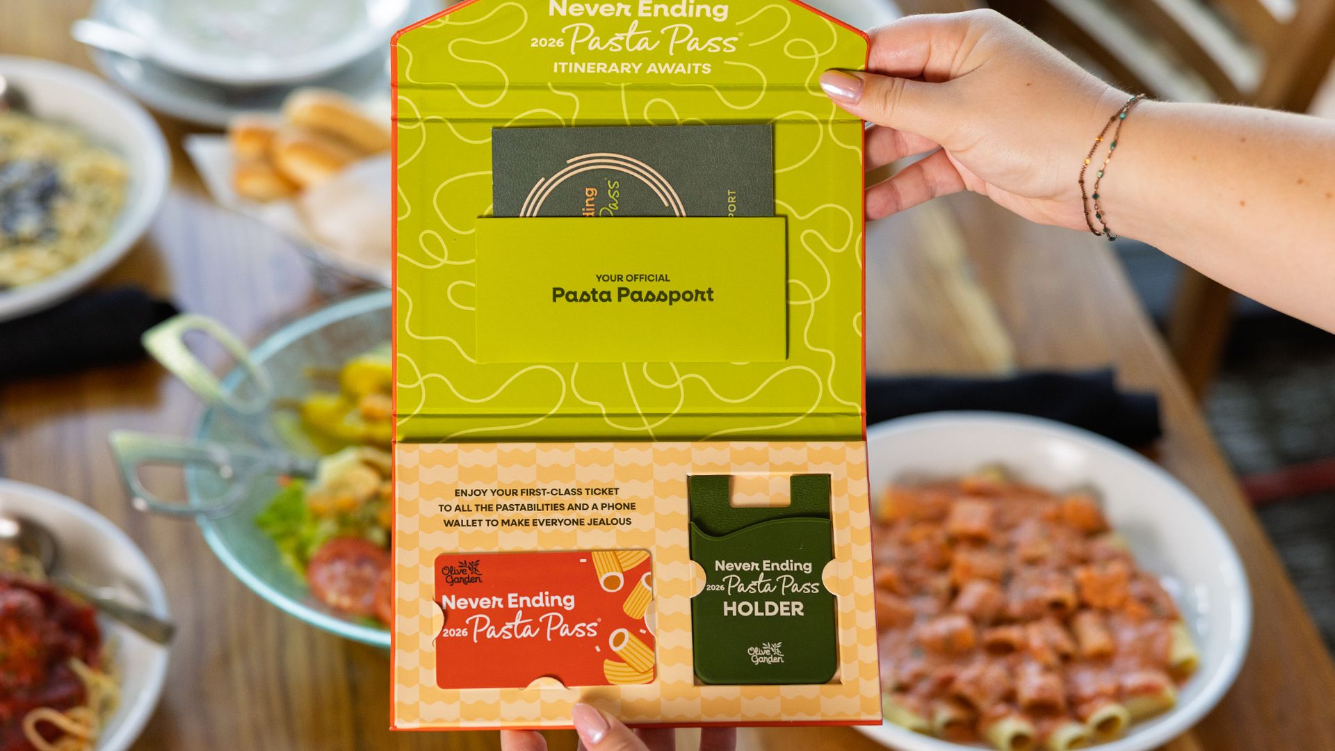 A hand holds a neon lime-green promotional display reading "Never Ending Pasta Pass," revealing a "Pasta Passport" card; blurred bowls of pasta sit on a wooden table in the background.