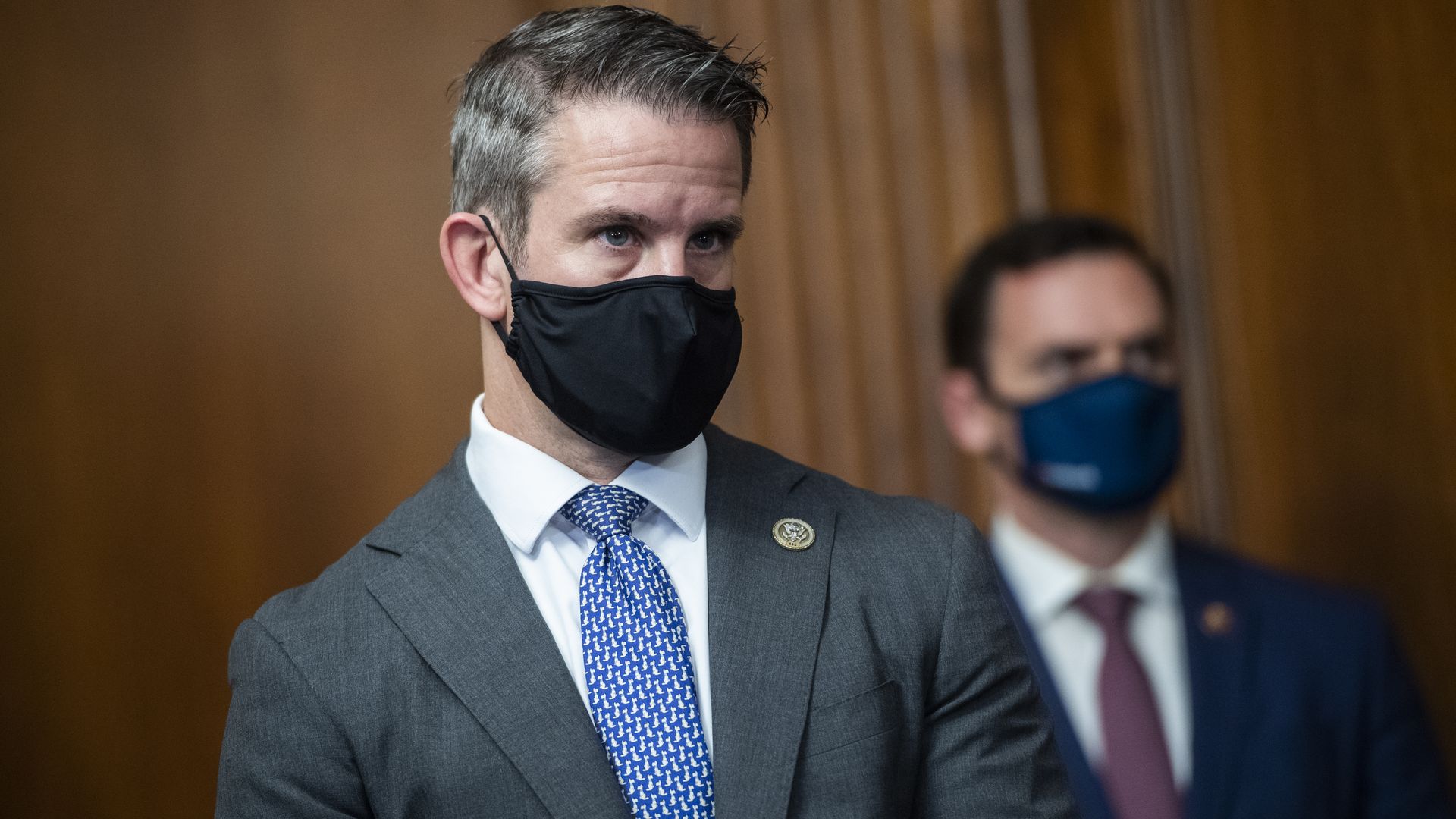 Kinzinger wears a face mask and a suit and tie 