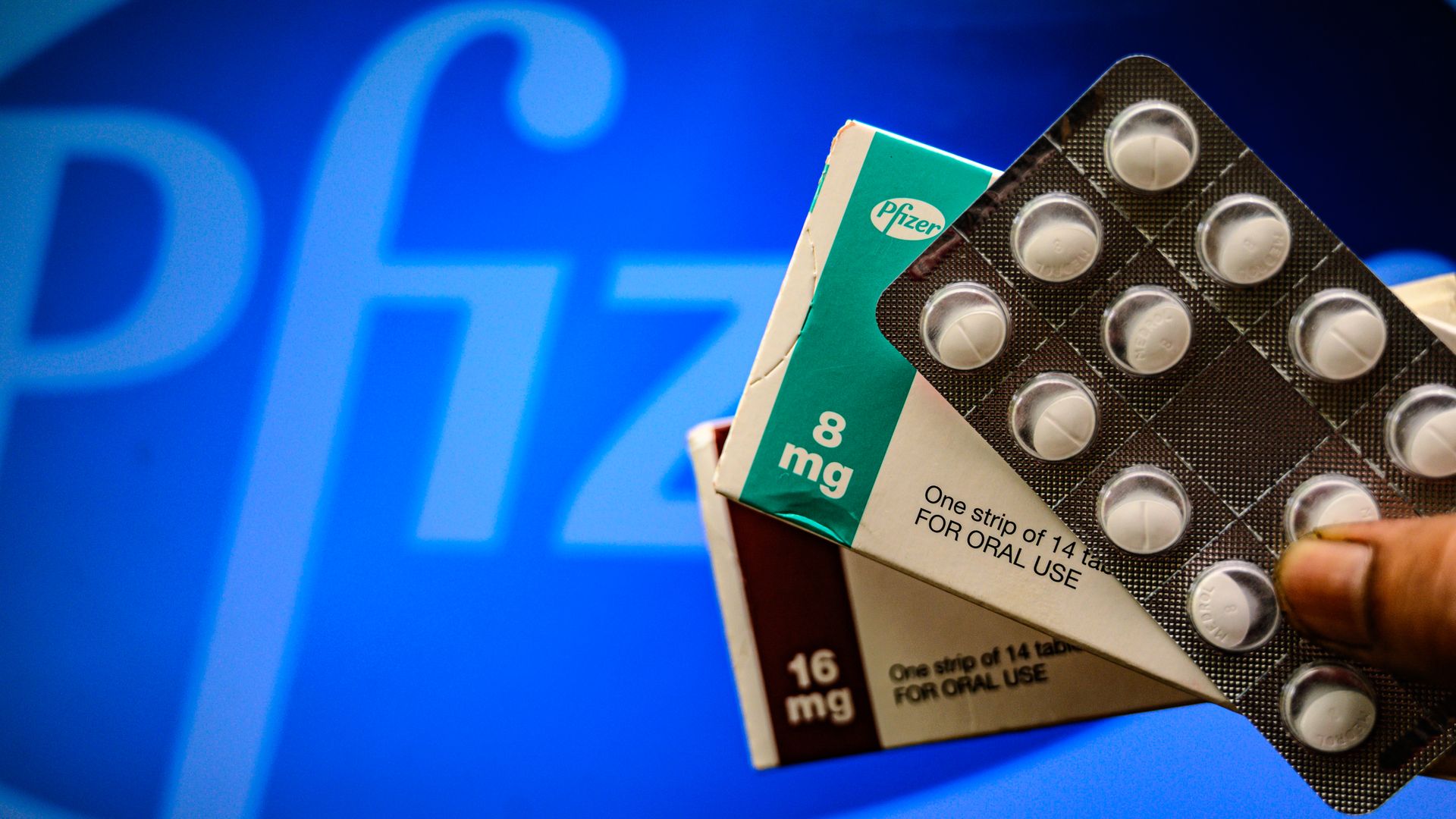 Pills being held in front of the Pfizer logo