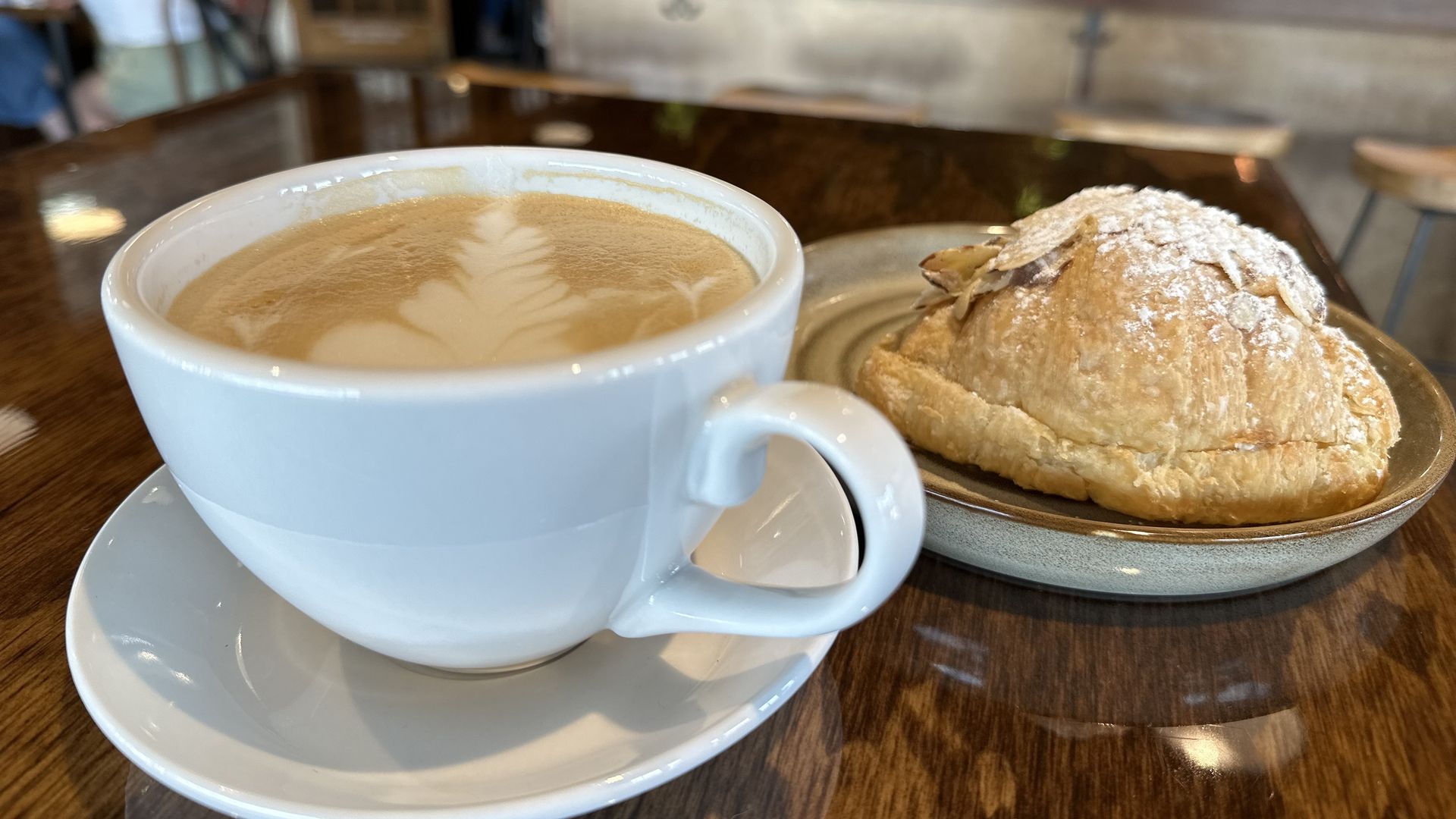 A latte in a white mug next to a pastry on a plate