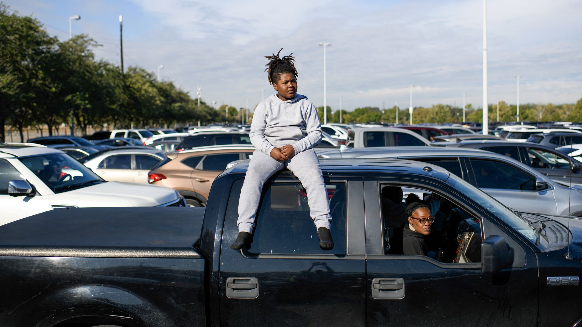 A child sits on top of a pickup as a family waits in line for food assistance