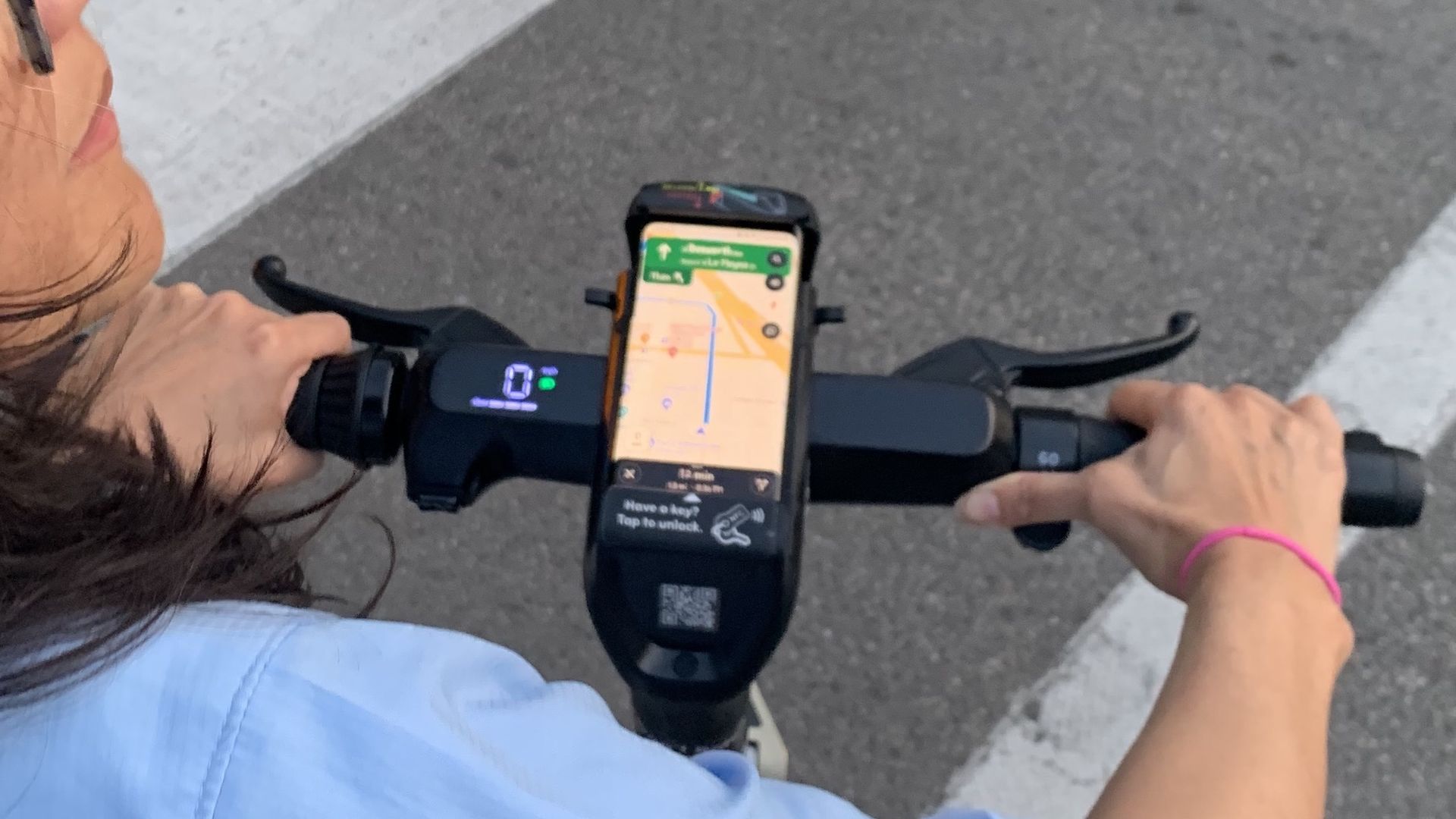 Photo of a woman riding a scooter with her phone on the handlebars. 