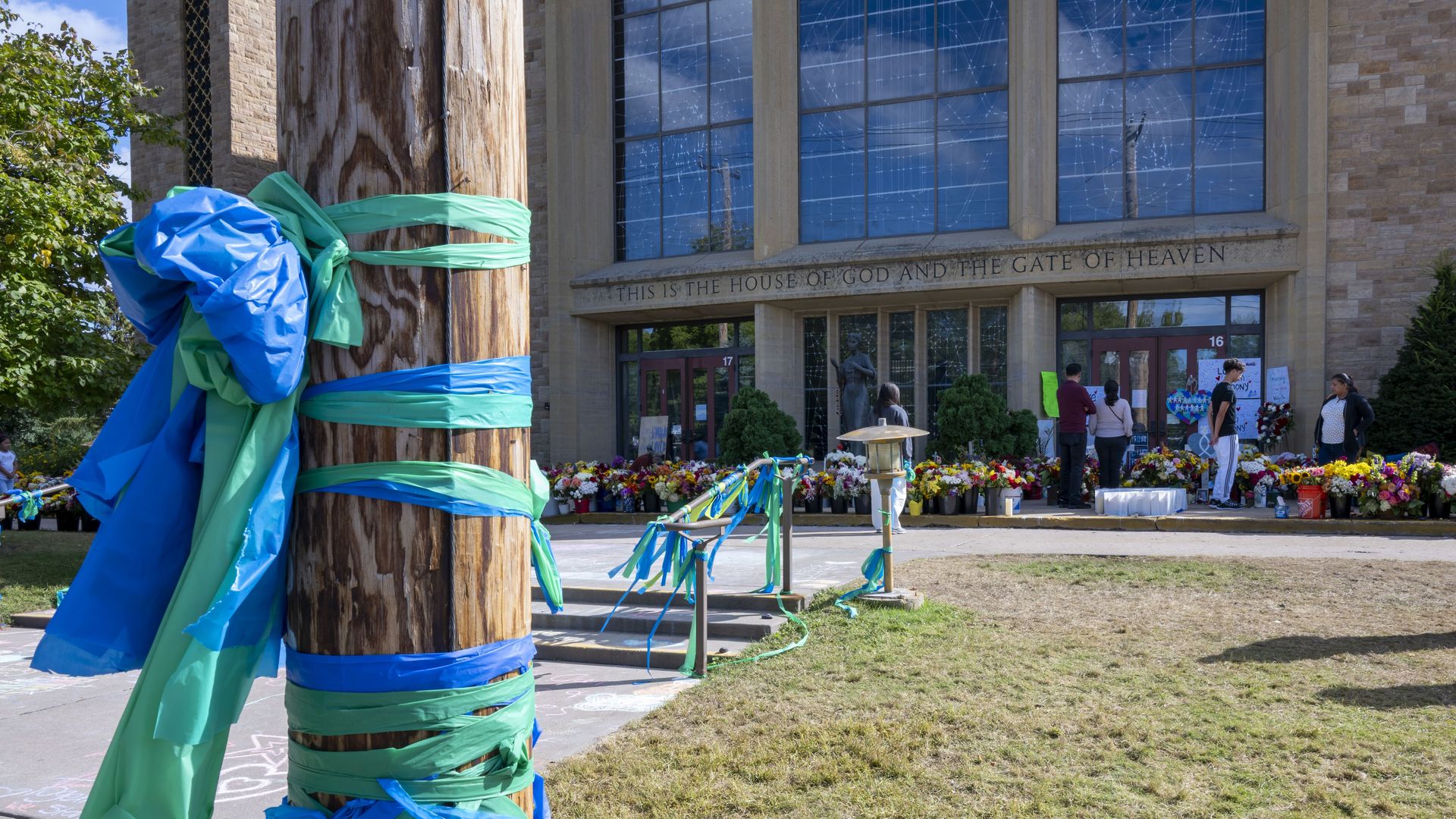 A memorial at Annunication church with blue and green ribbons around a pole and flowers at the doors