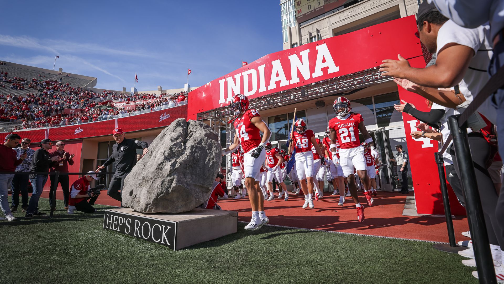 The Indiana football team walking out onto the field in front of a rock 