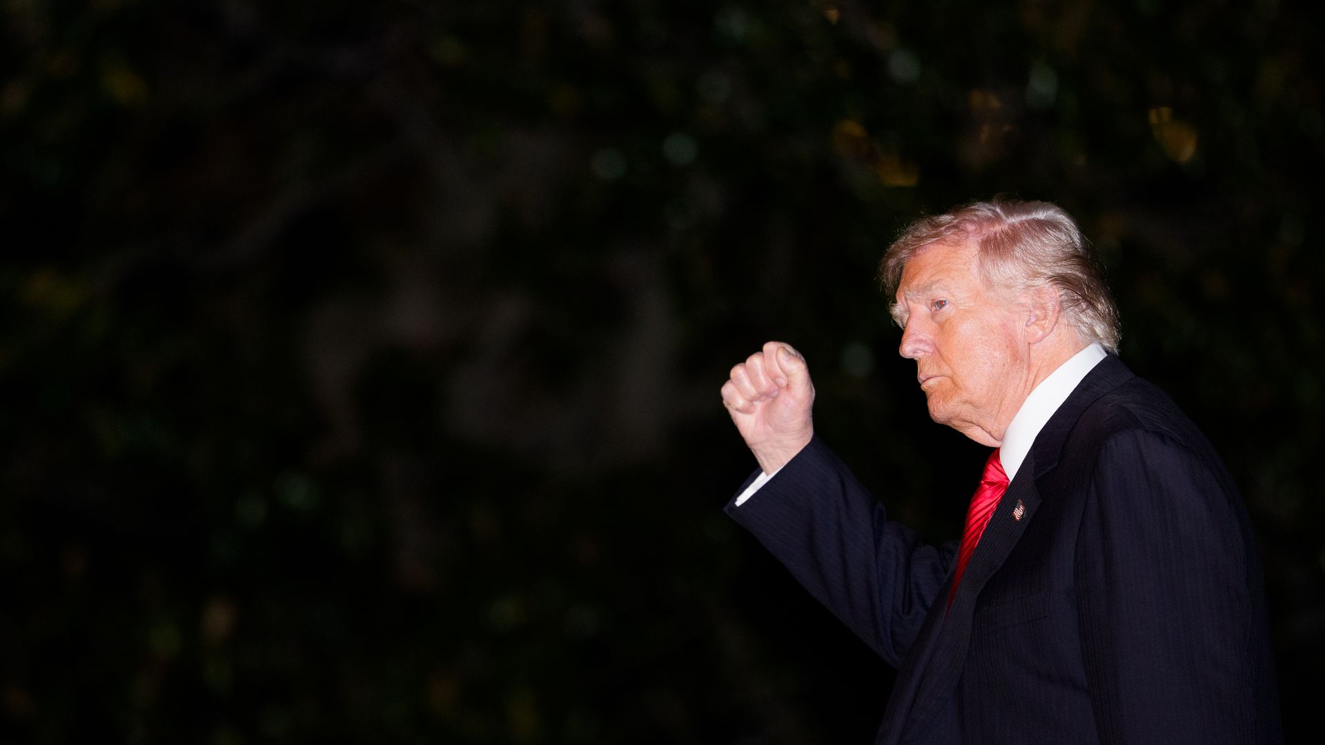 President Trump, wearing a dark suit, white shirt and red tie, holds a fist up as he walks