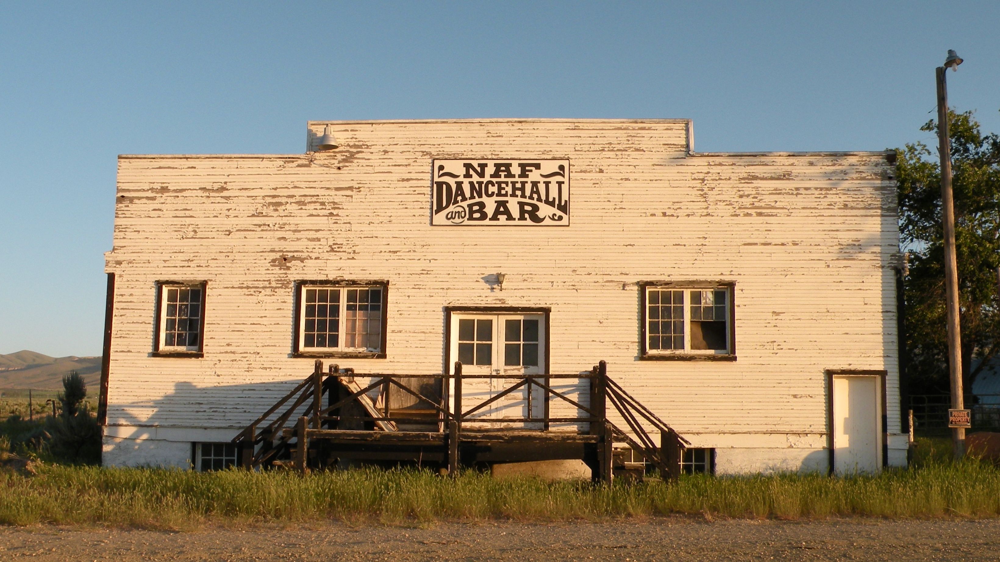 A white wooden building with a false front facade and a sign reading "Naf Dancehall and Bar"
