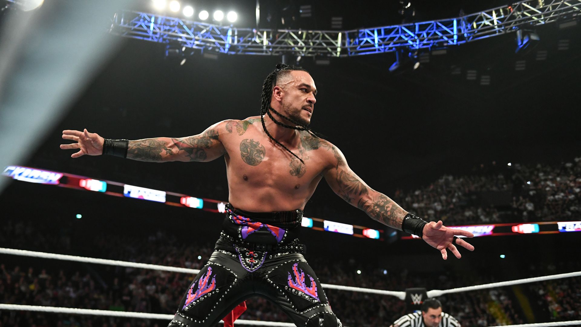 Wrestler Damian Priest stands inside a ring with his arms spread out, looking down