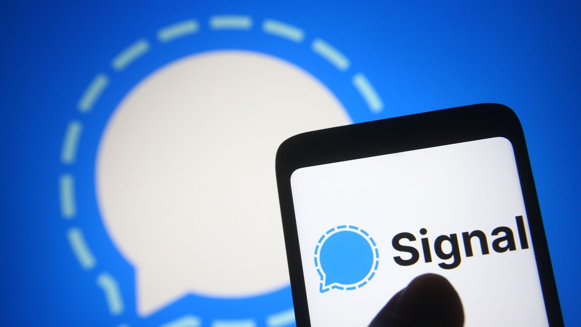 A photo illustration of the Signal logo on a smartphone against a Signal logo backdrop