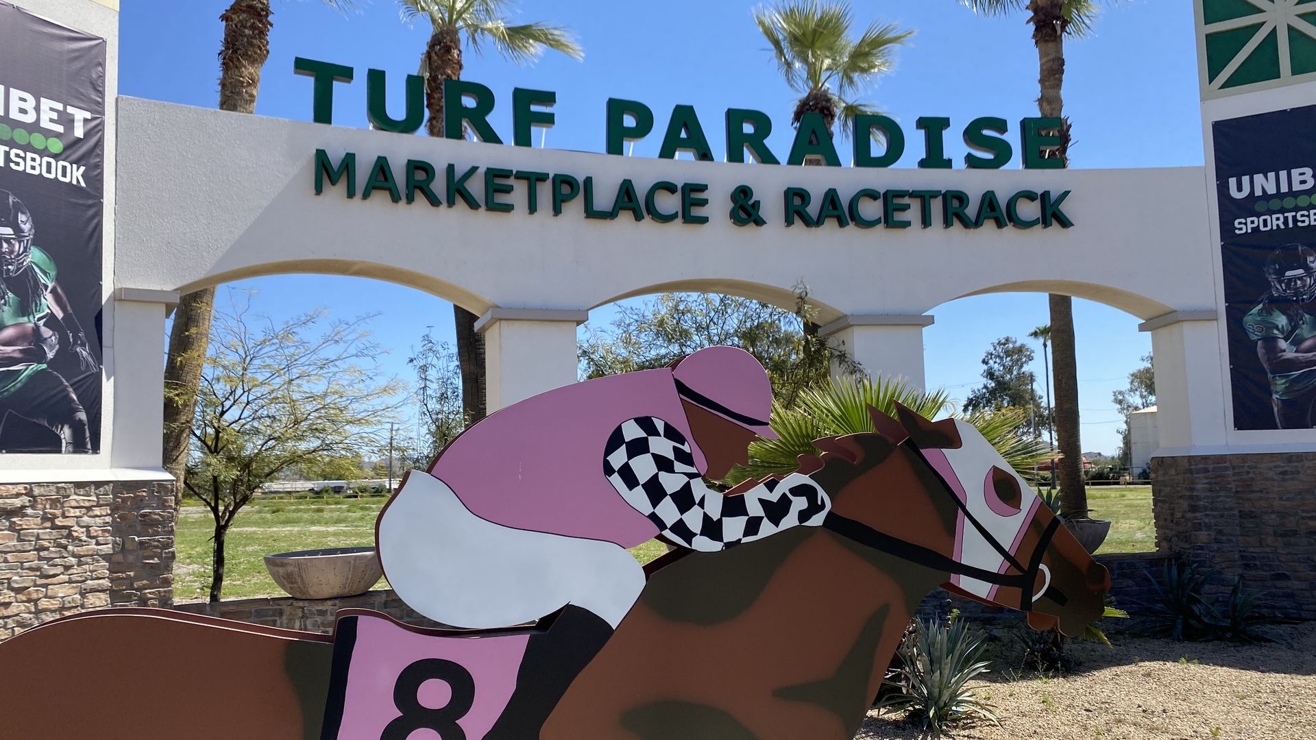 A sign that reads Turf Paradise Marketplace and Racetrack behind a figure of a jockey on a horse.