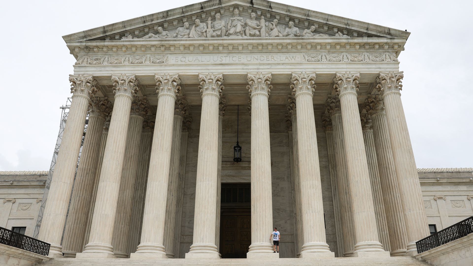 Photo shows the exterior of the U.S. Supreme Court with a tourist standing on one of the pillar bases.