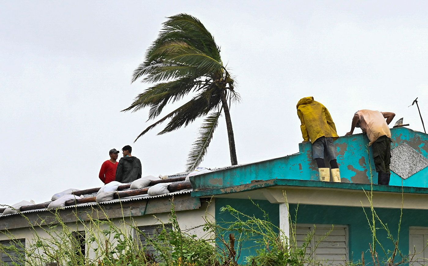 Men sitting on a roof repairing it after Hurricane Ian