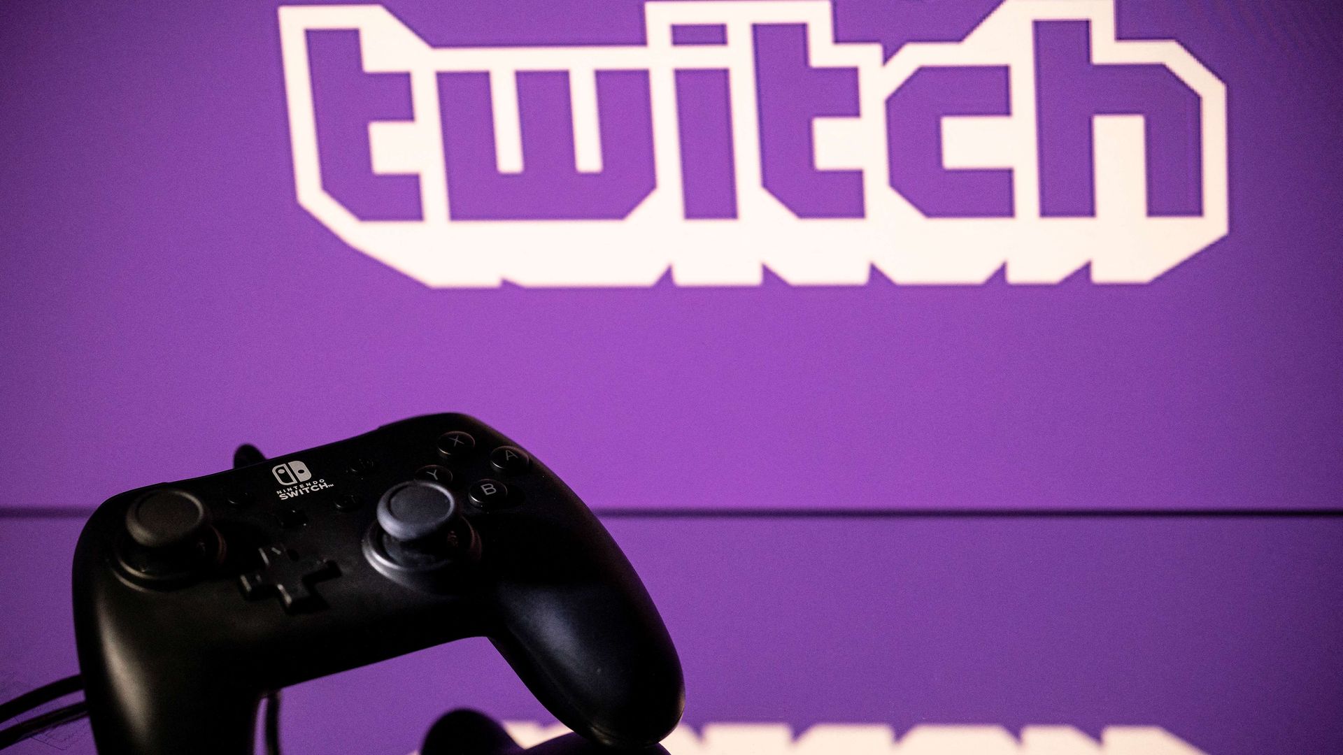 Photo showing a black gaming console set in front of a large screen with the purple Twitch logo