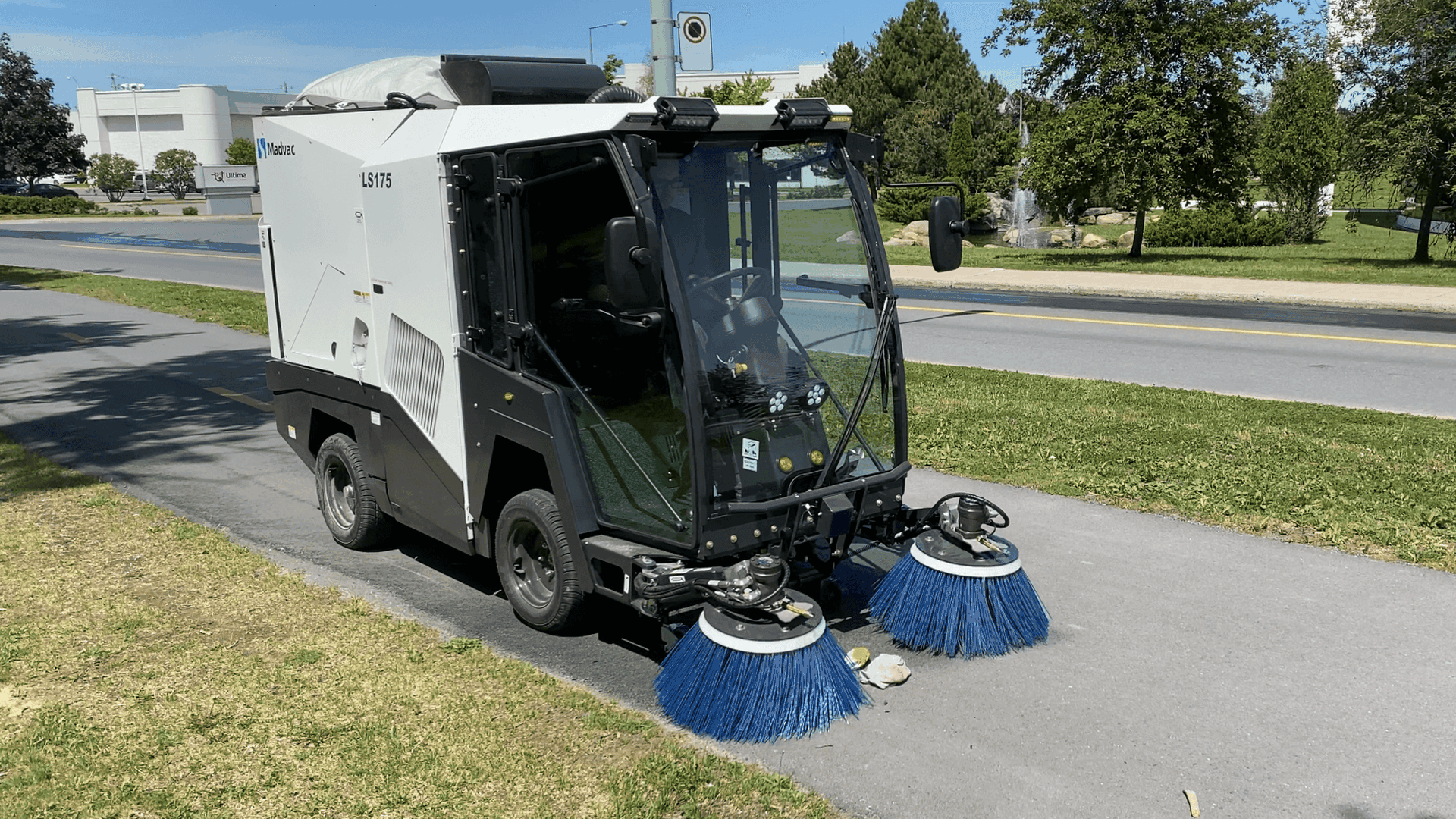 Photo of a narrow street sweeper cleaning a sidewalk 