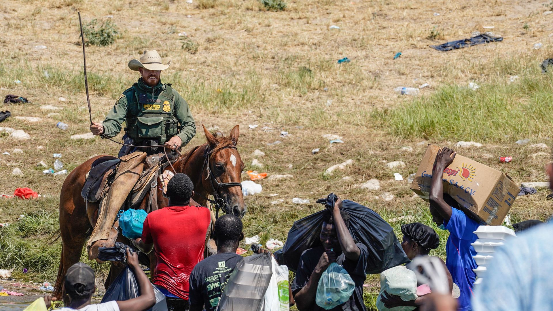 Photo of a Border Patrol agent on a horse swinging his whip as he faces a group of Haitian migrants waist deep in the Rio Grande River