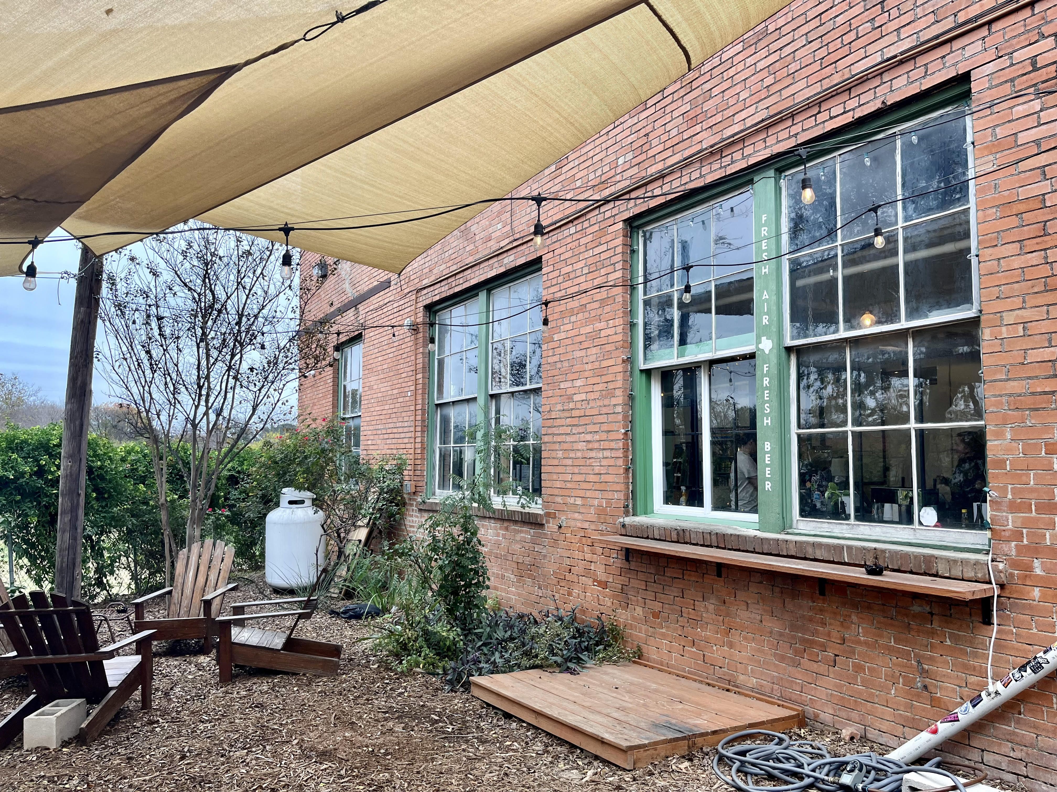 A brick wall with a walk-up window and outdoor patio chairs.