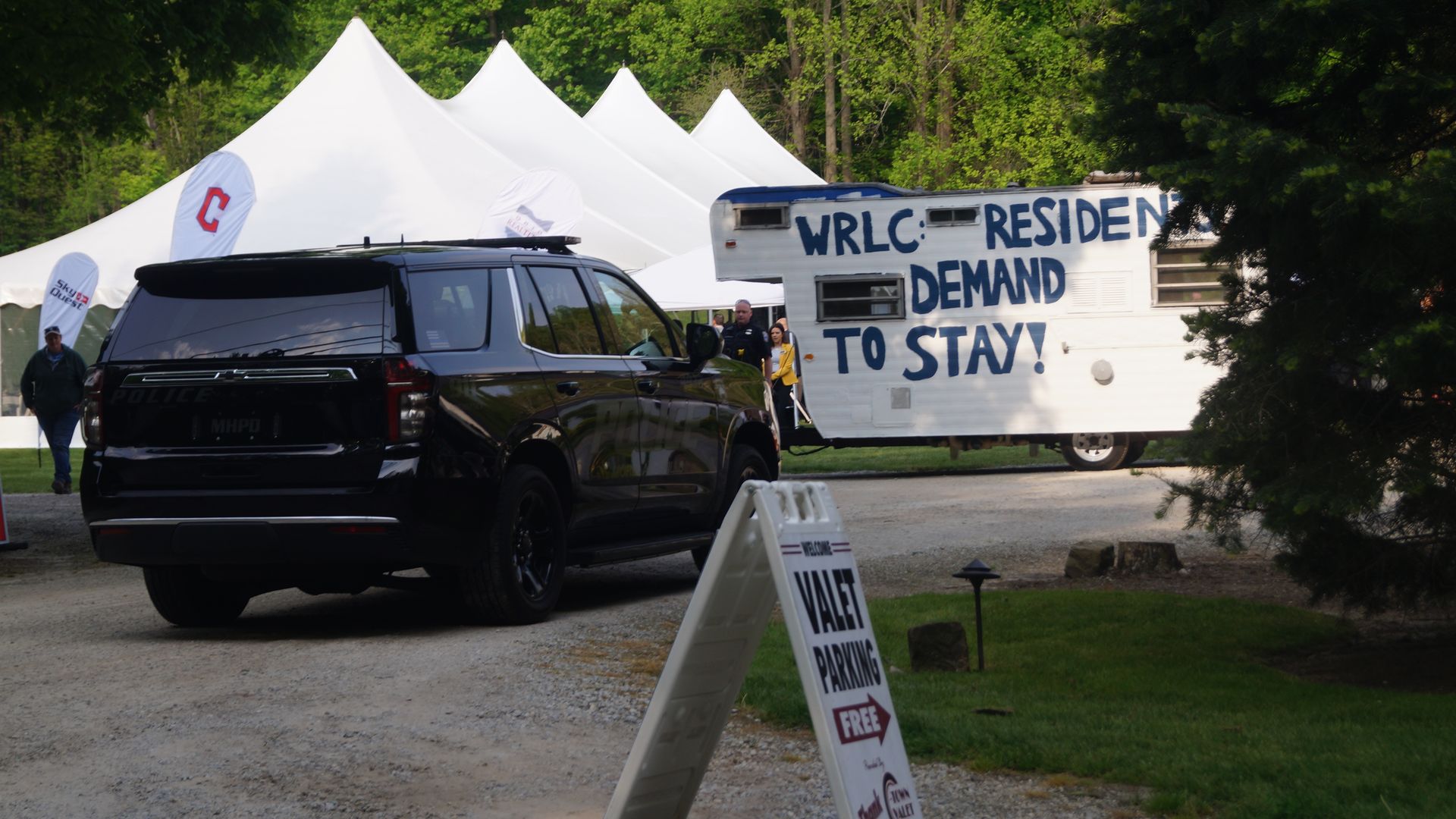 A trailer painted with the message, "WRLC: Residents Demand to Stay" with outdoor tents in the background an police SUV in the foreground