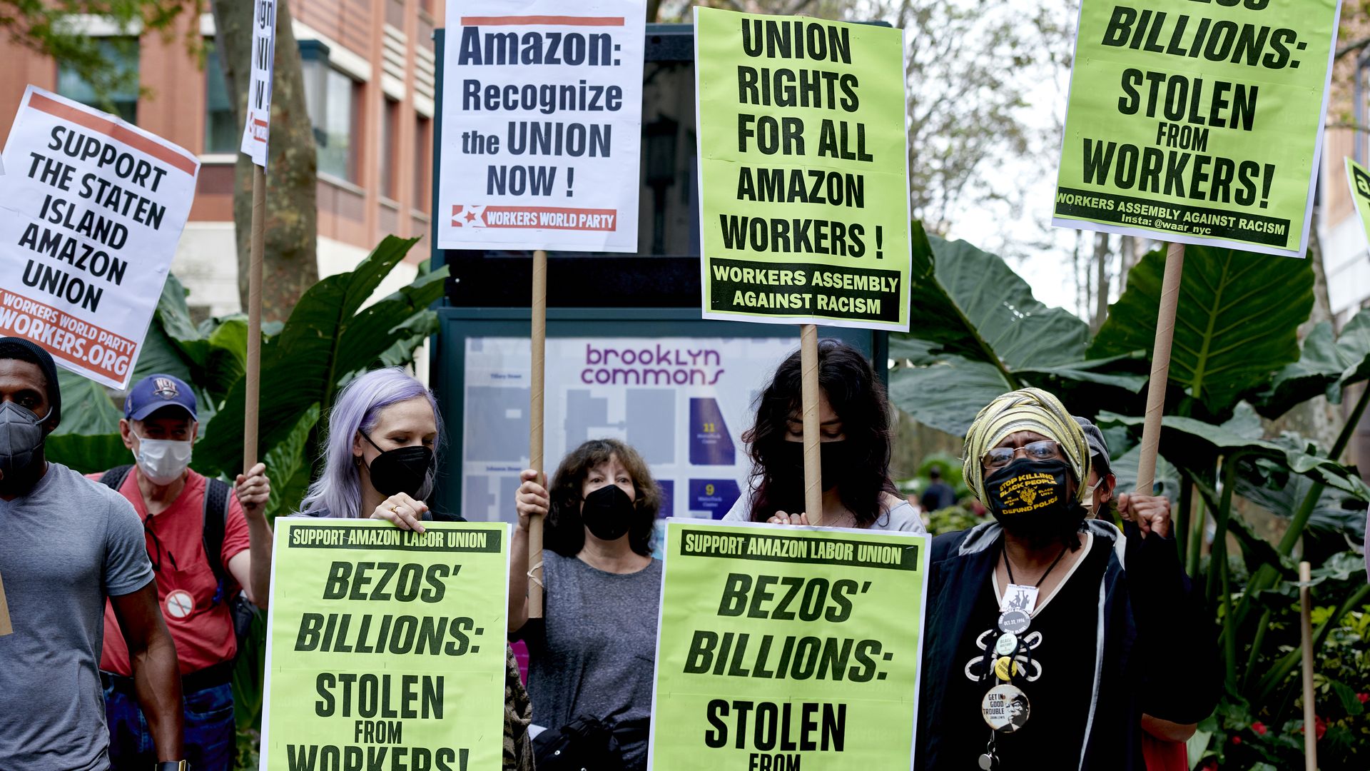 Photo of protesters holding up signs that say "Bezos' billions: stolen from workers" and "Amazon: recognize the union now!" in an outdoor rally