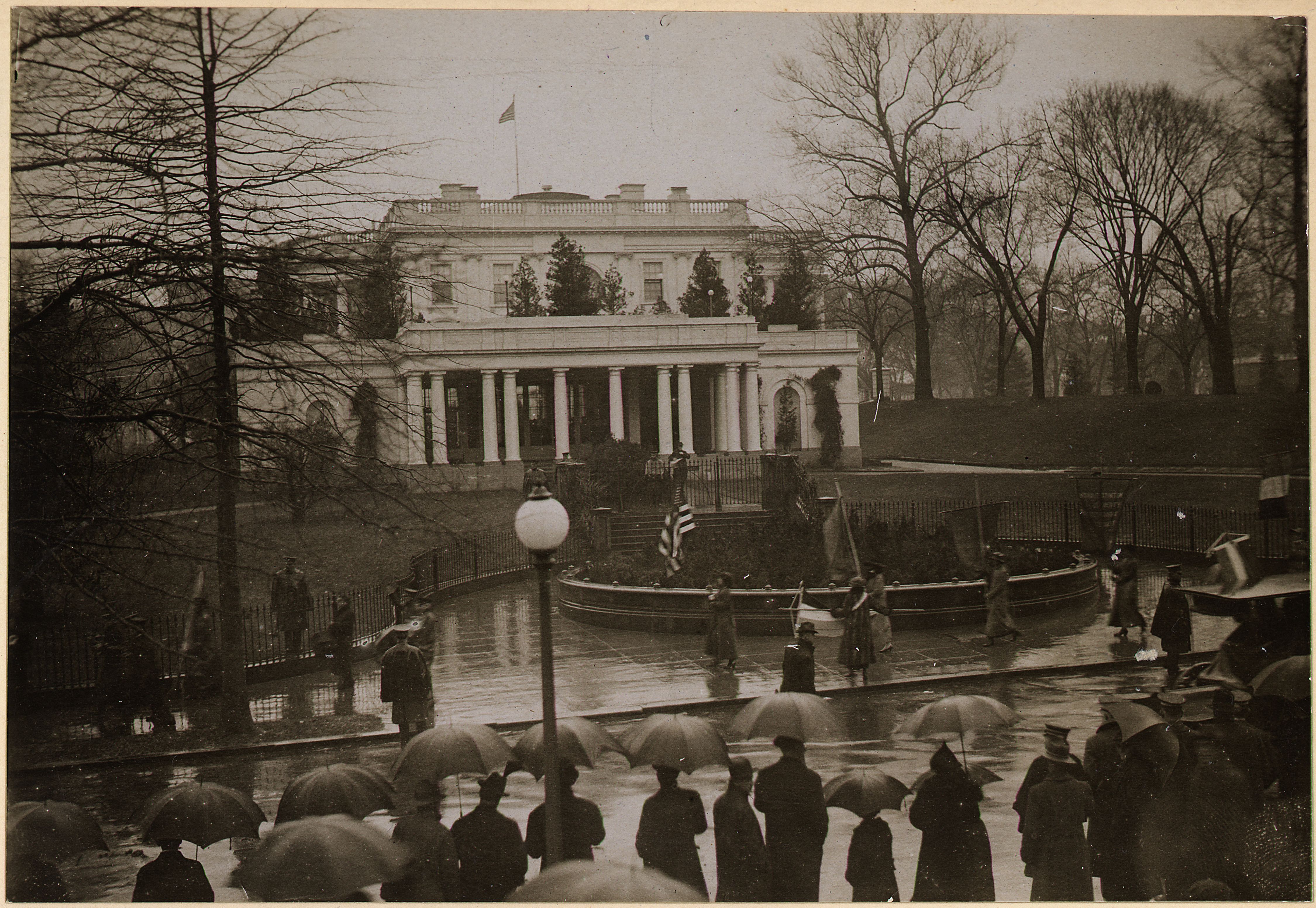 Suffragists, carrying banners, on picket duty at the East Entrance of the White House in this black and white photo from 1917.