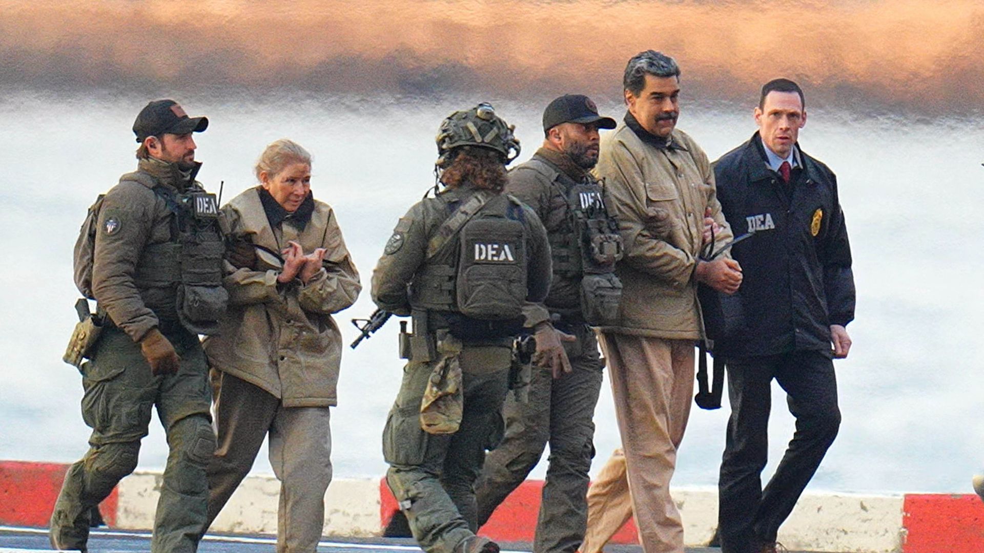 Nicolás Maduro and his wife, both of whom wear khaki jackets and pants, are escorted by a group of people in DEA uniforms. 