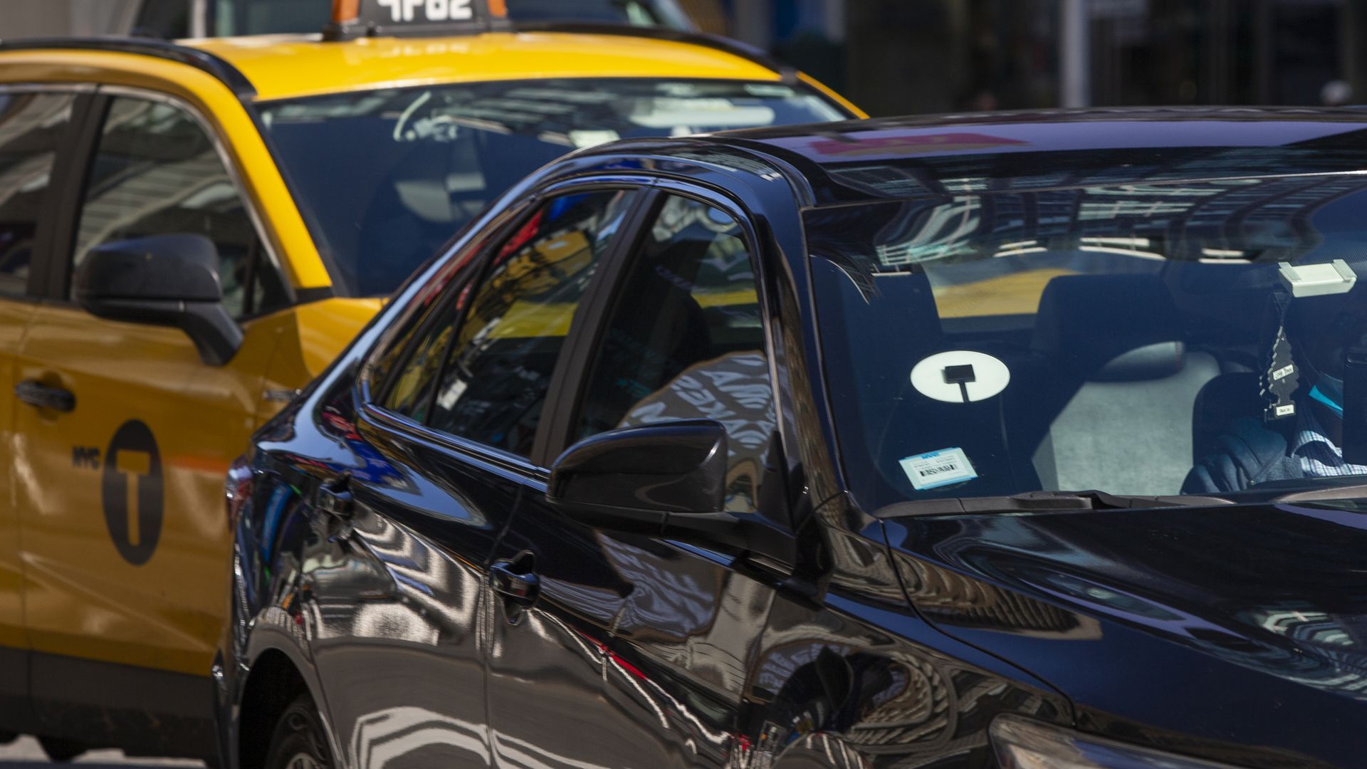 A photo of an Uber and yellow taxi next to one another