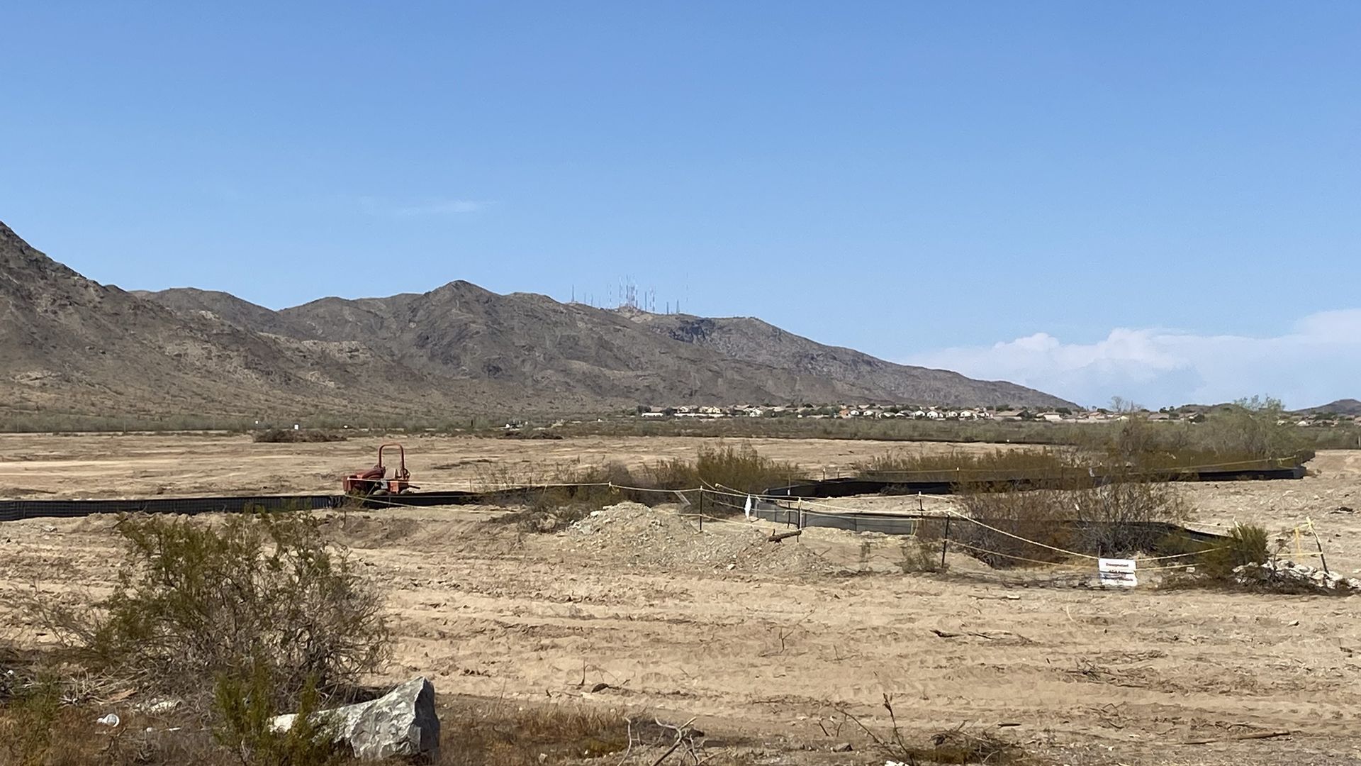 A vacant desert lot with a mountain and houses in the background.