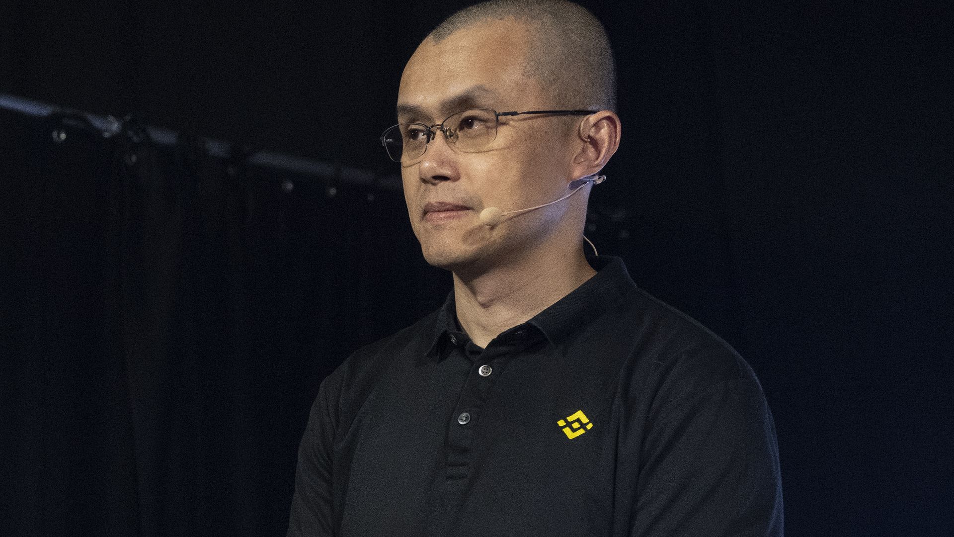 A photo of CZ waiting to speak at a conference, wearing his Binance shirt. 