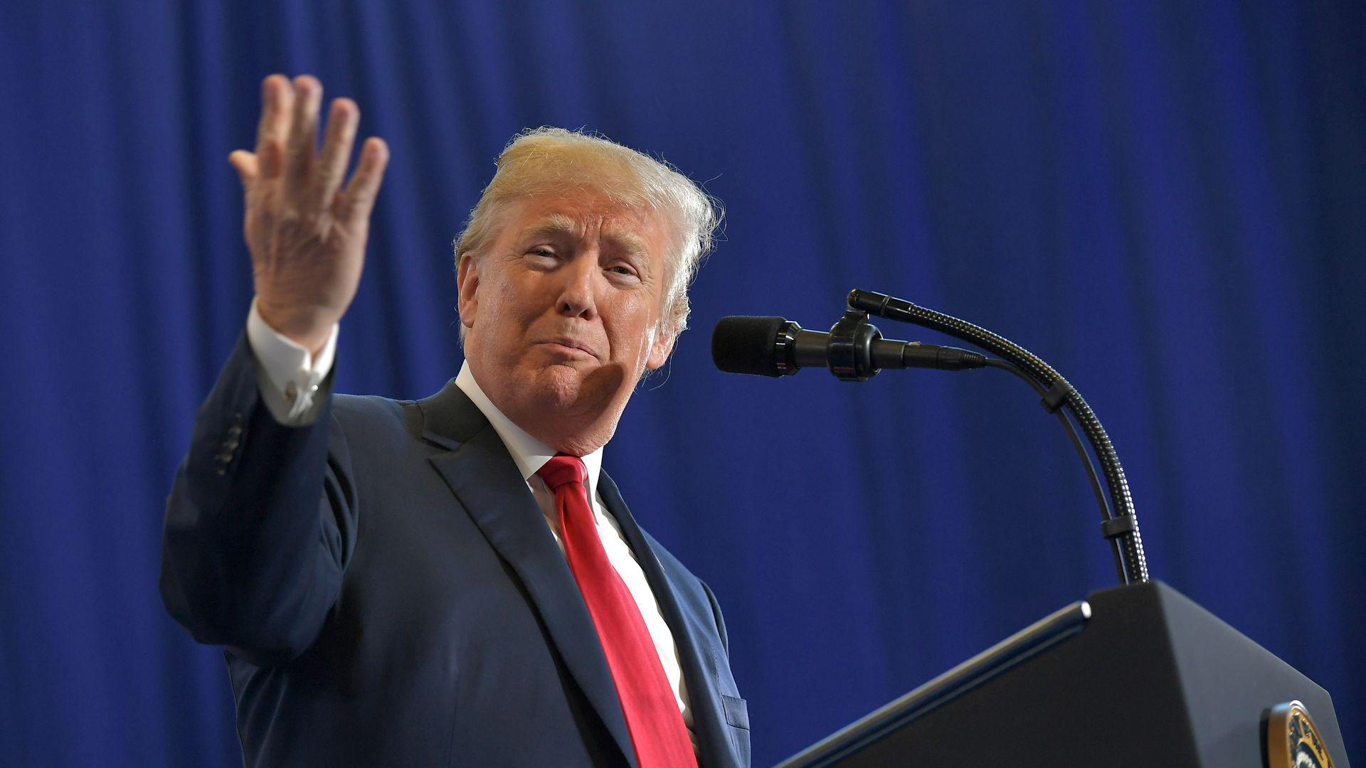 Donald Trump lifting hand at mic with red tie and navy suit