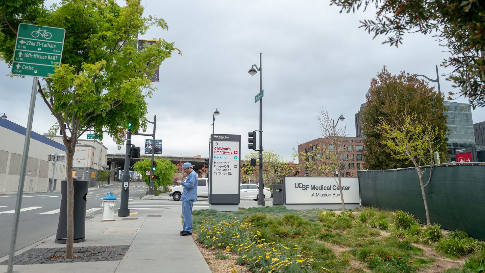 A medical provider in blue scrubs stands outside UCSF Medical Center at Mission Bay