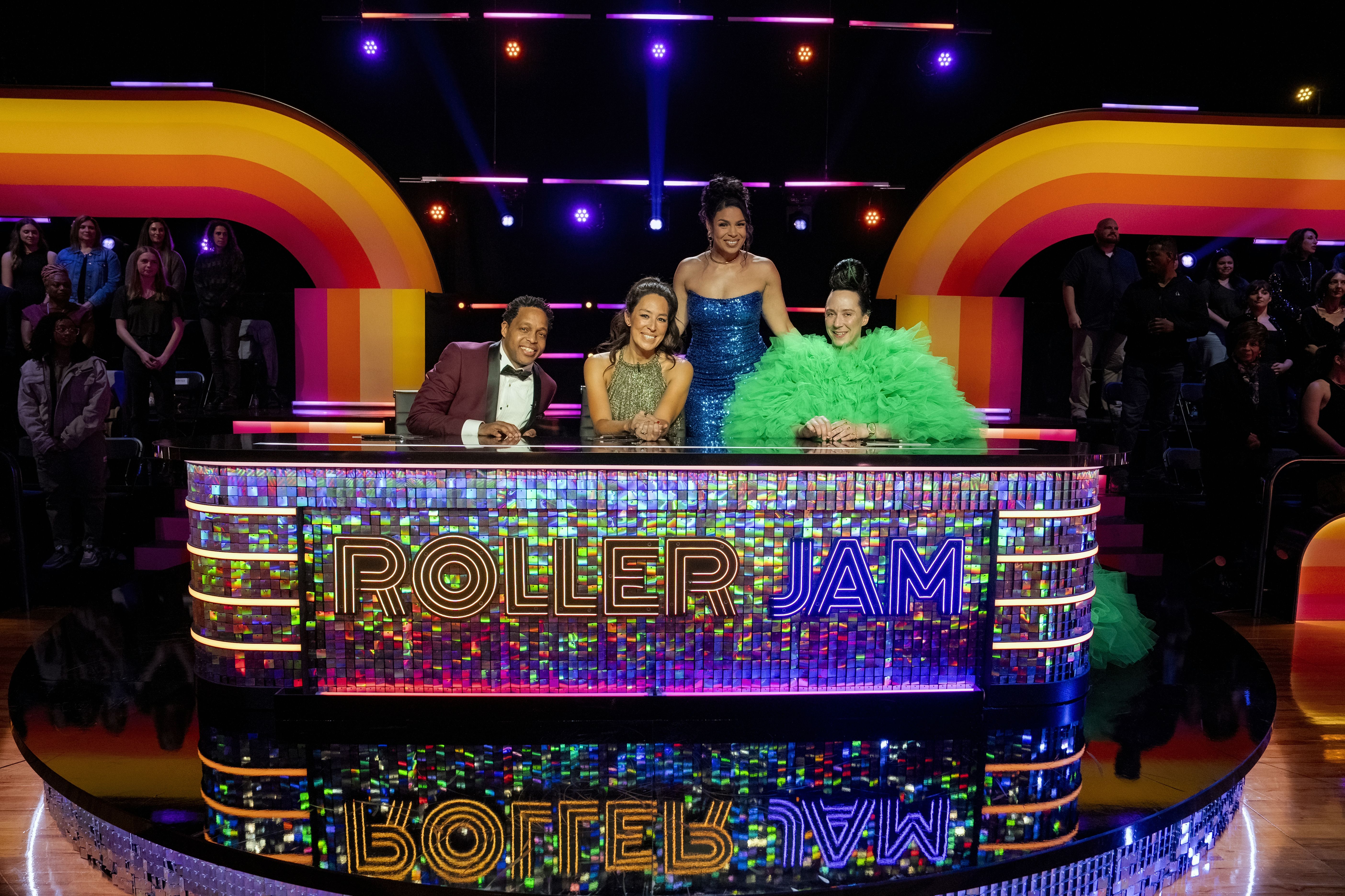 Four people pose for a photo while seated behind a large lit-up desk that says "Roller Jam" on the front.