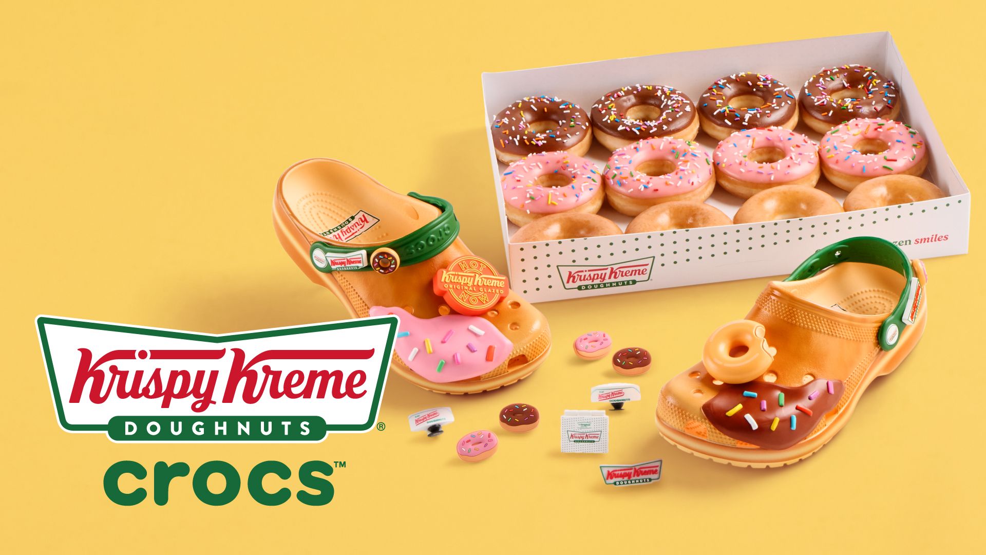 Orange Crocs decorated with Krispy Kreme doughnut charms, placed next to a box of assorted chocolate, pink, and original glazed doughnuts on a yellow background with Krispy Kreme and Crocs logos.