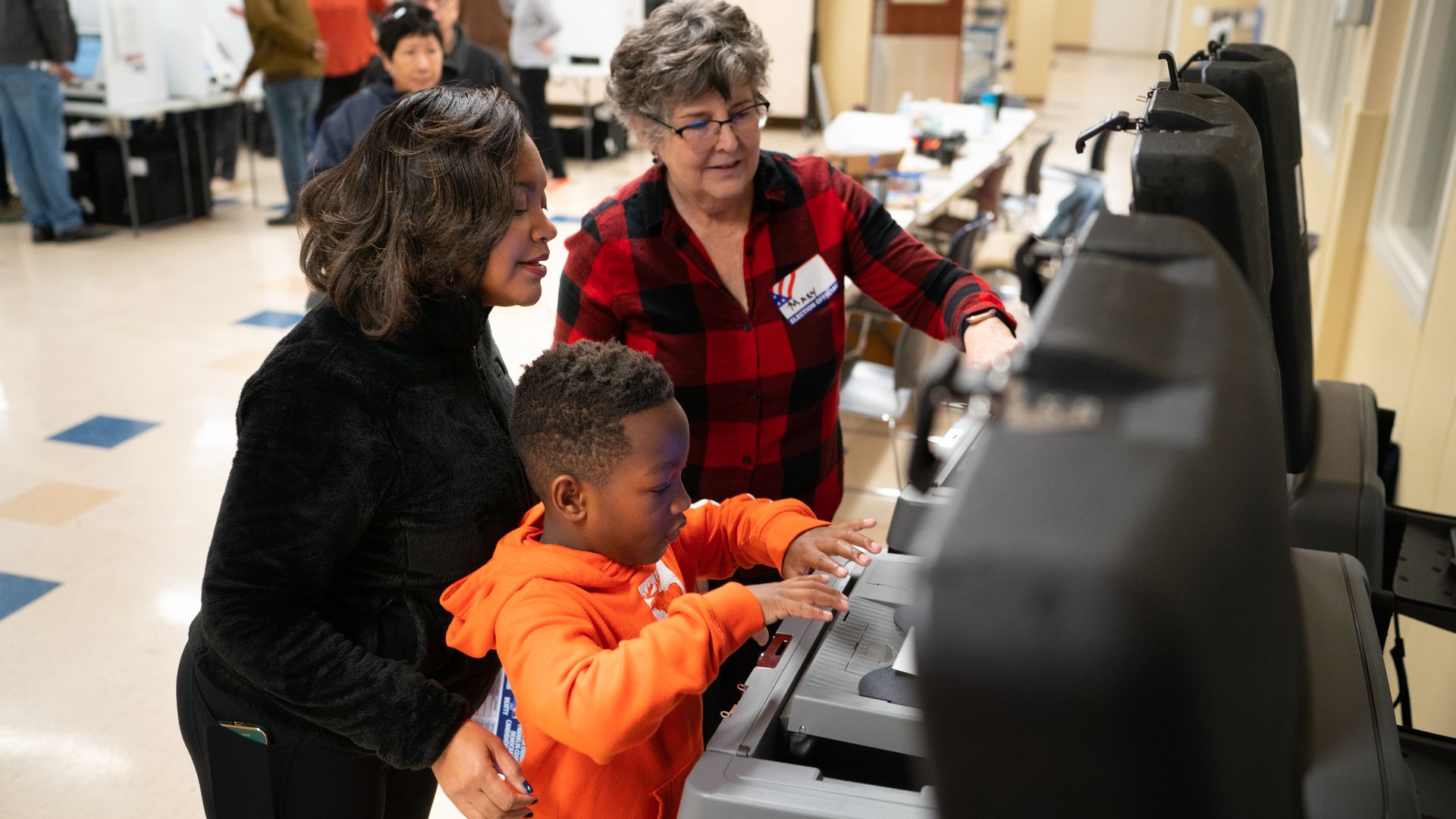 A poll worker helps a woman and child place a ballot into a ballot reader. 