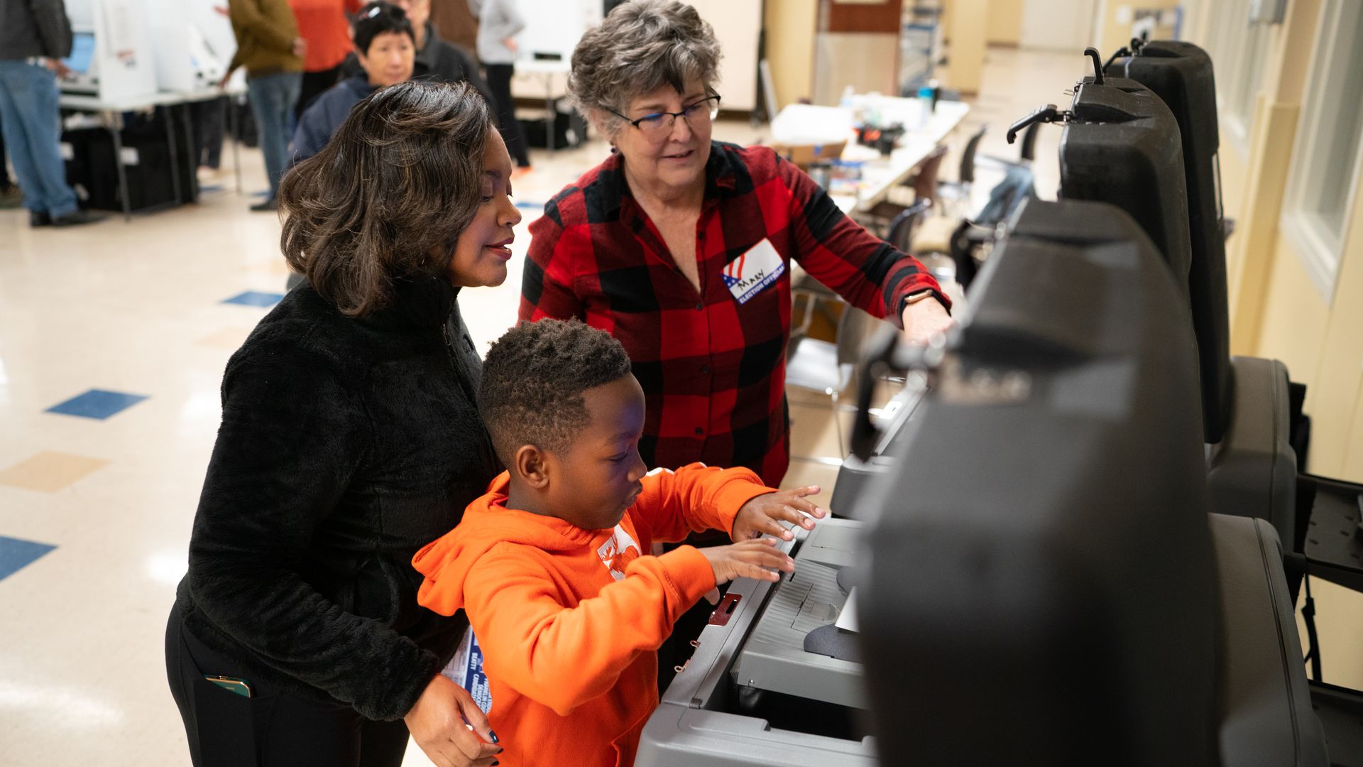 A poll worker helps a woman and child place a ballot into a ballot reader.