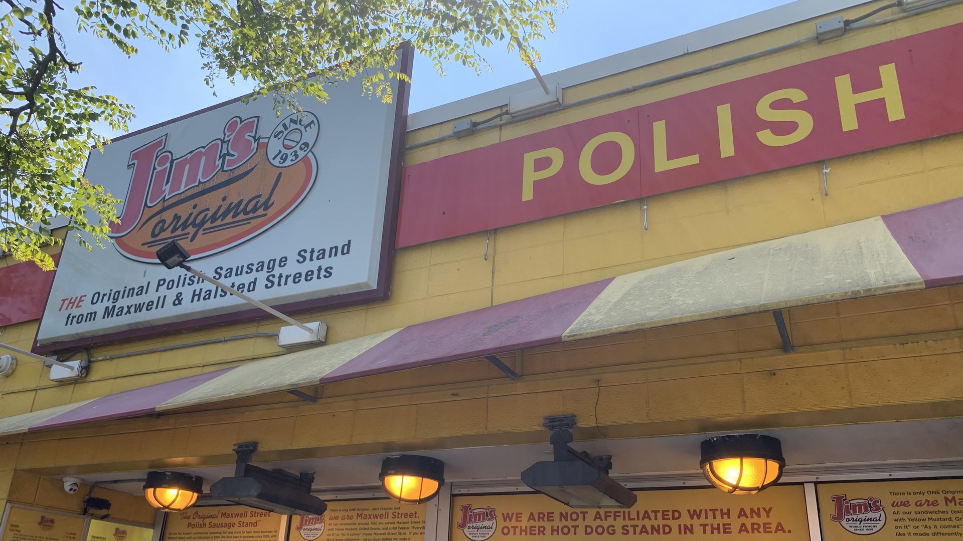 Bright yellow storefront with a large red POLISH sign on the facade and a white sign reading "Jim's original" with a circular logo. Menu boards and customers line up outside on a sunny day.