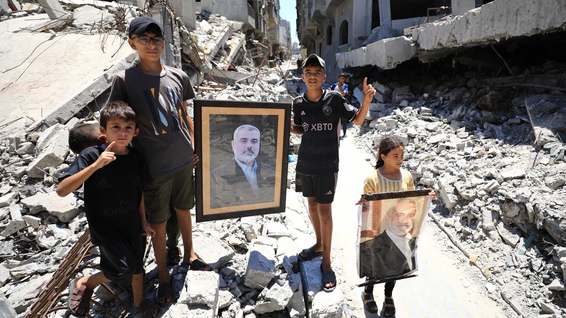 Palestinians carry the portrait of Hamas political bureau chief Ismail Haniyeh, who was assassinated, as they stand on the debris of destroyed building belonging to Haniyeh, following an Israeli attack in Al-Shati refugee camp of Gaza City, Gaza on July 31, 2024. 