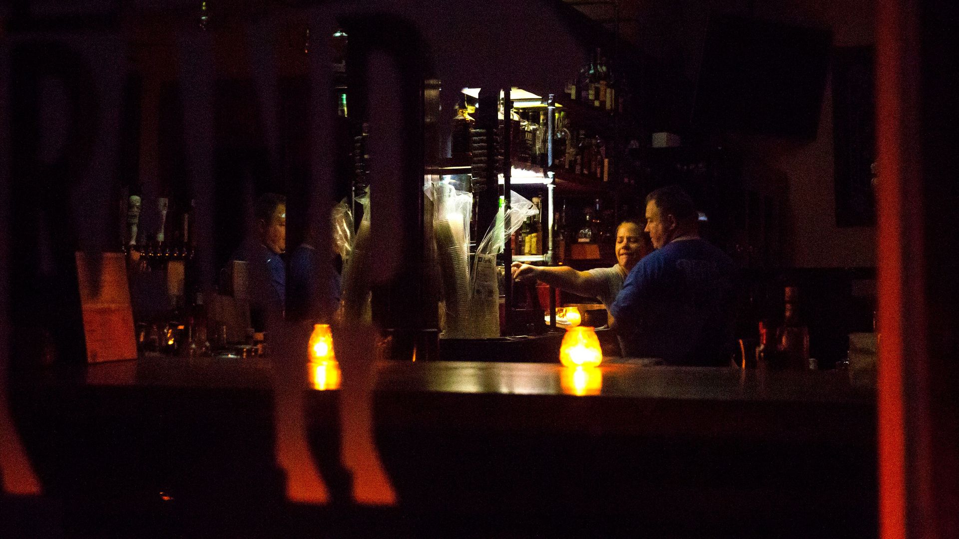 In this image, a bartender serves a customer at a darkened bar.