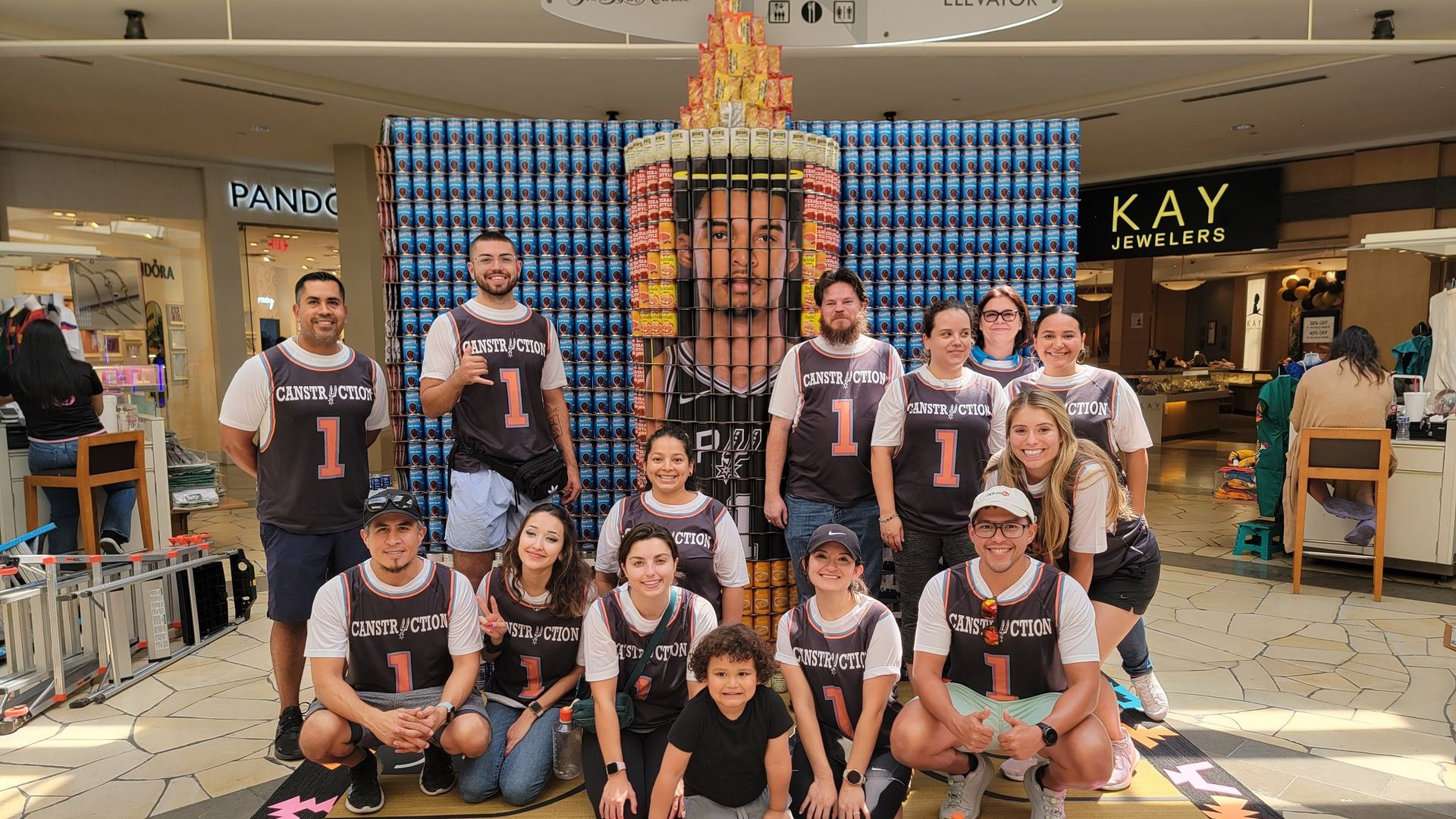 A group of people stand in front of an arrangement of canned goods designed to be a prayer candle.