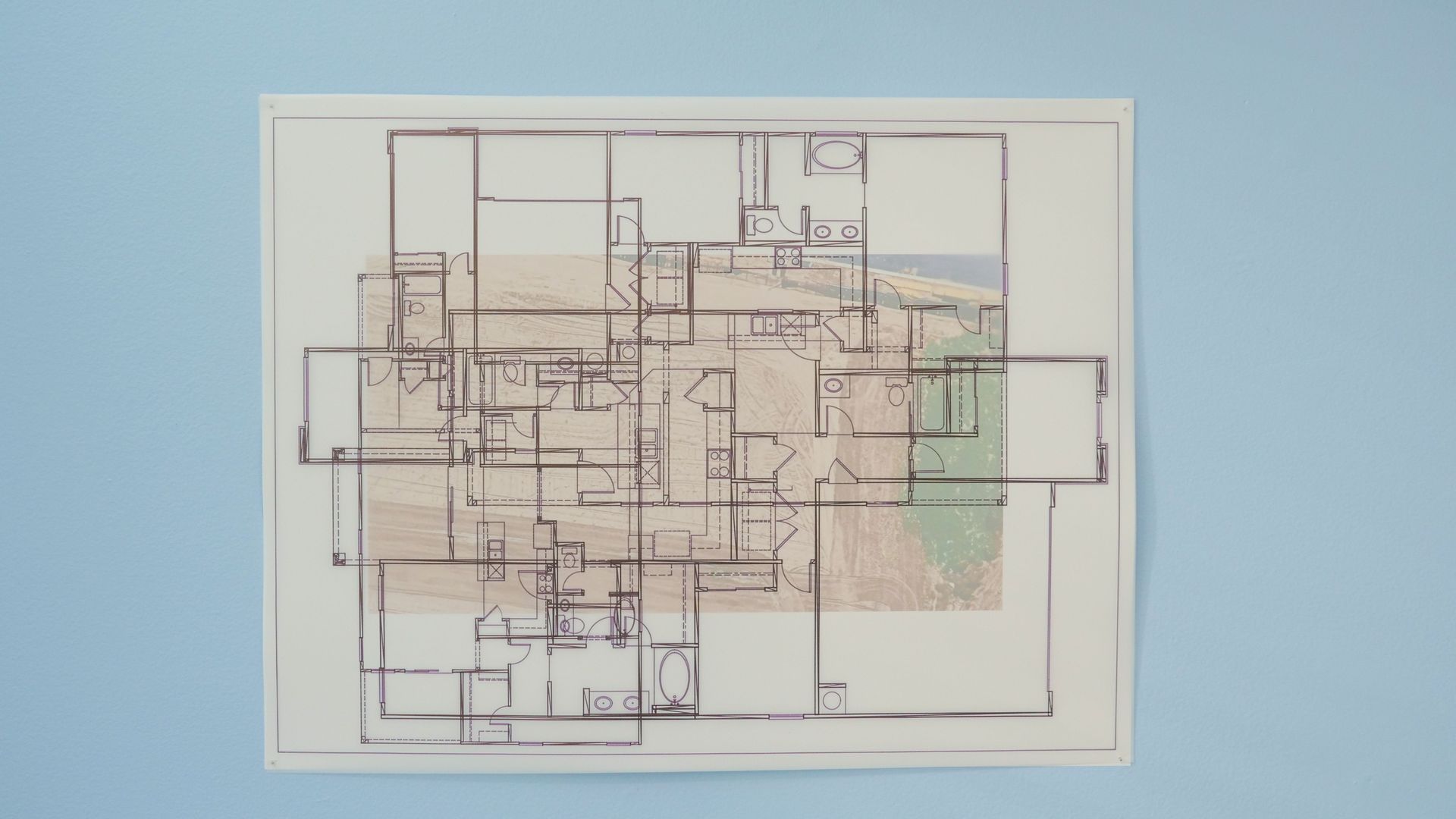 Large architectural blueprint showing a multi-room floor plan with doors and fixtures, printed on white paper mounted on a pale blue wall.