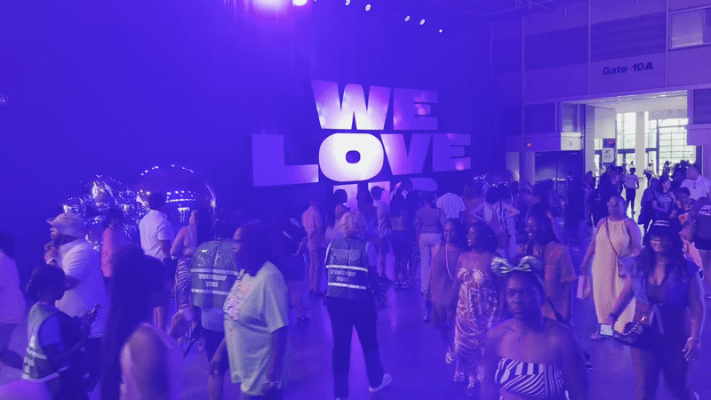 People walk past a purple-lit area with a large text display that says "We love us."