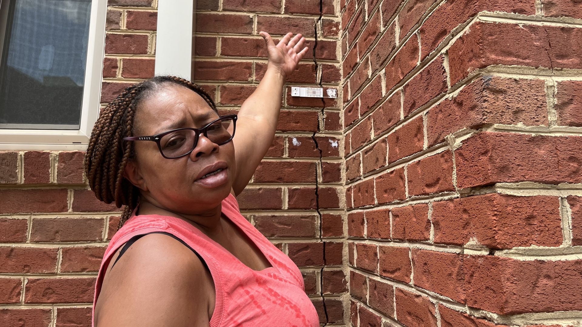 Homeowner points to a crack in the brick facade of building