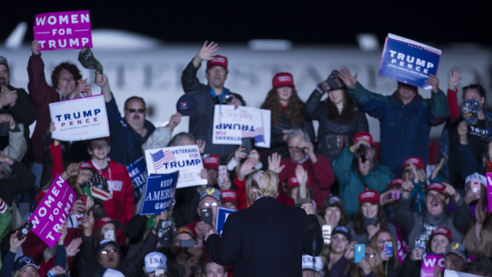 In this image, Trump faces a wall of supporters at a rally. Supporters hold signs that say: "Women for Trump" and "Trump Pence" 
