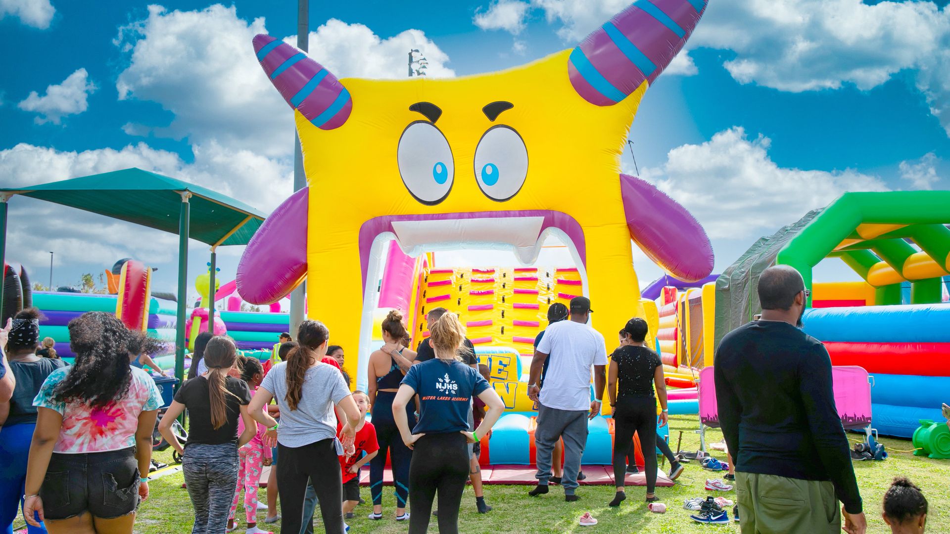 People standing outside a giant inflated square yellow face with a huge open mouth.