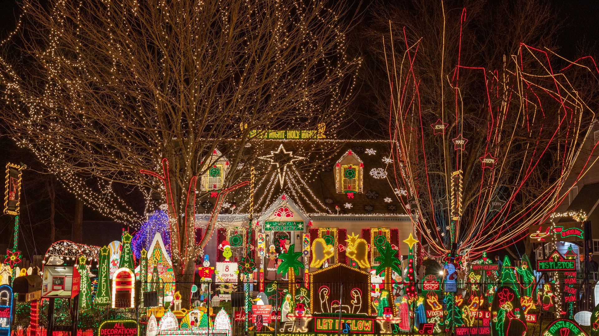 An all-decked out house with christmas lights in the trees, yard and on the house, plus lit up figures in the yard