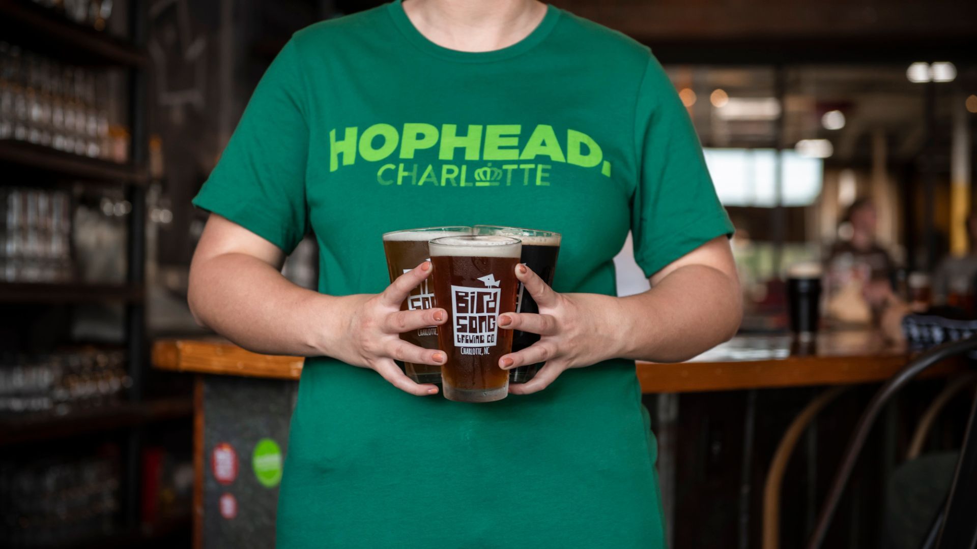 A person holding 3 beers and wearing a green shirt. 