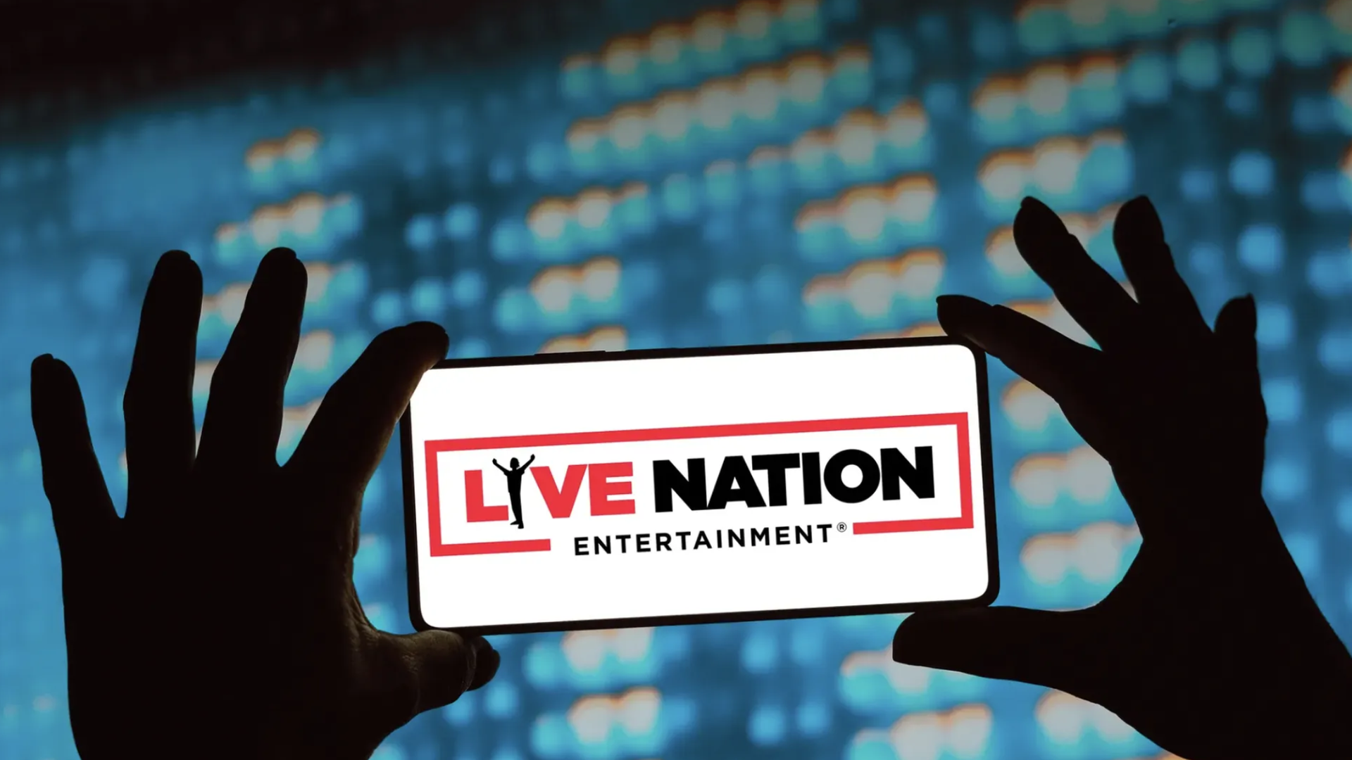 A photo illustration of two hands holding up a phone that says Live Nation Entertainment.