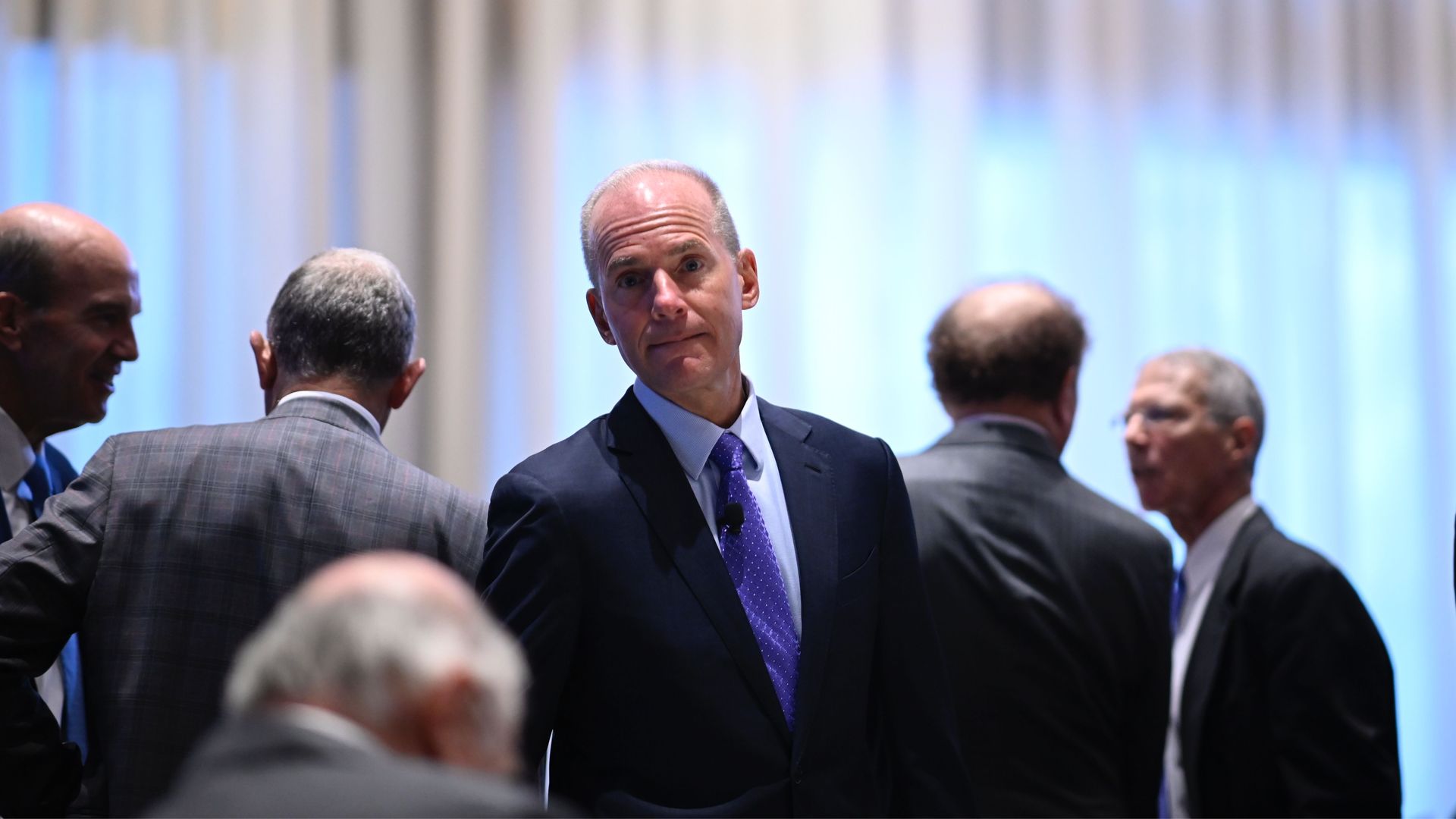 In this image, Muilenburg stands in the midst of a crowd that is facing the opposite direction. He is facing the camera.